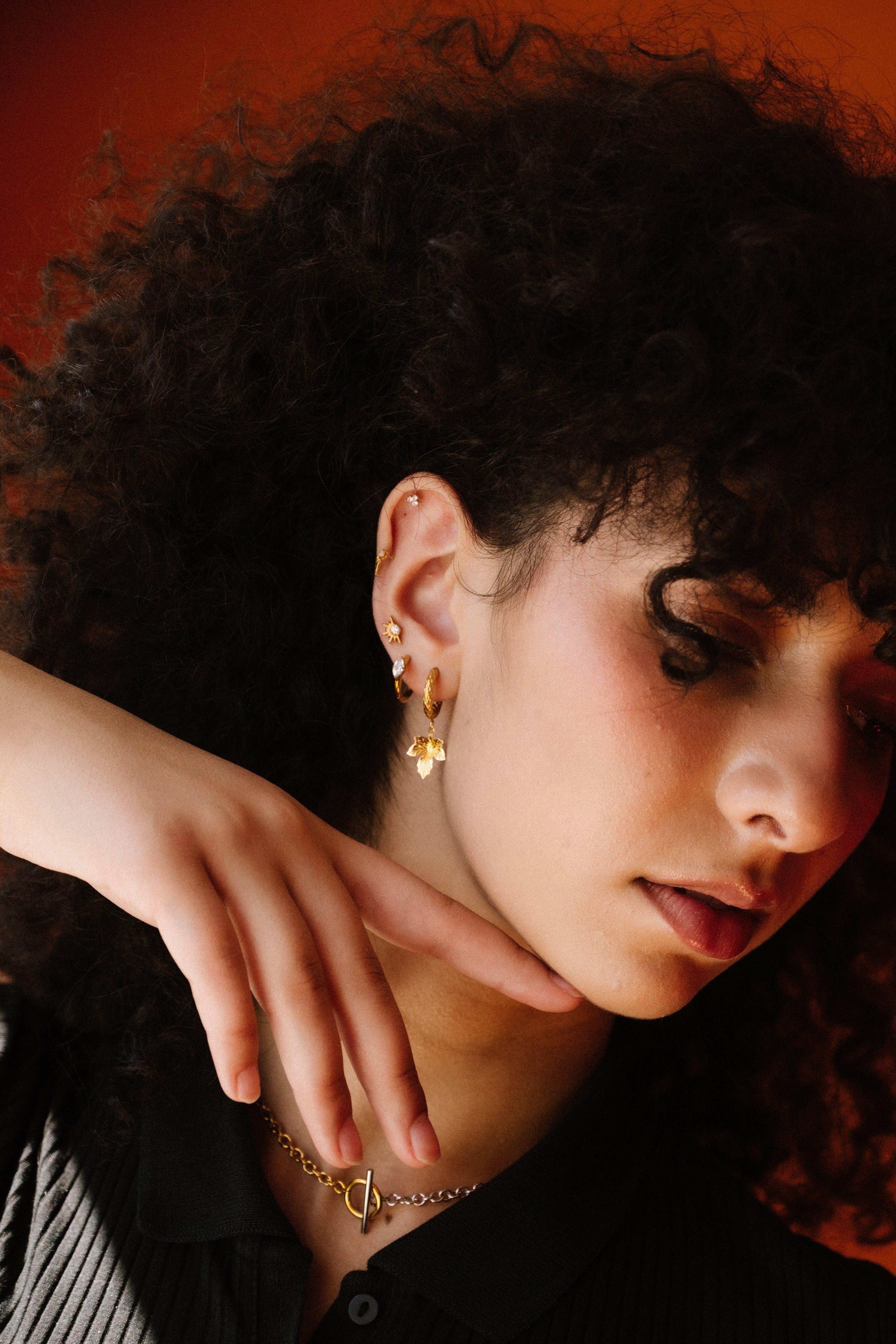 Woman with curly hair wearing gold earrings against an orange background