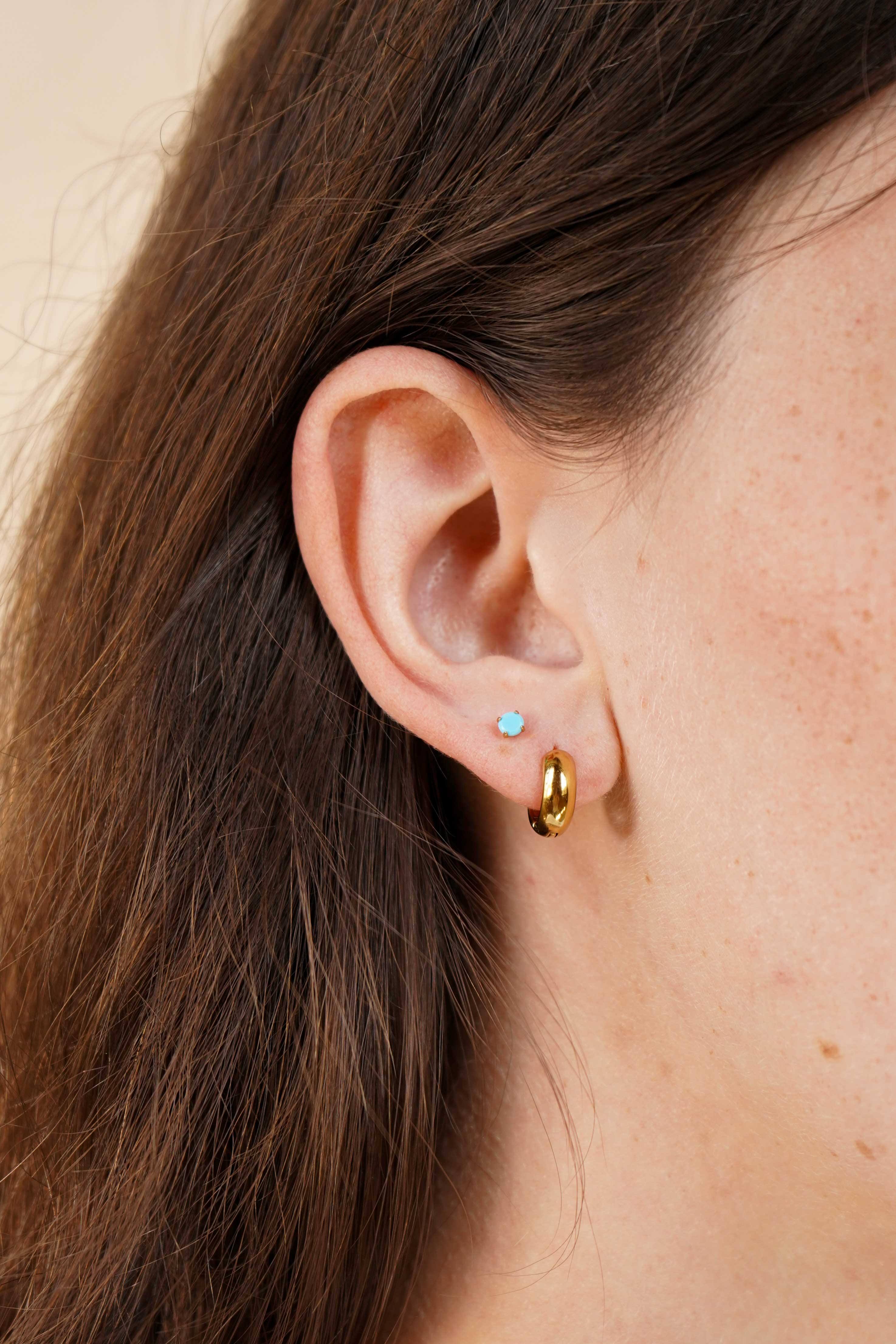 Close-up of an ear with gold hoop earrings and a blue gemstone earring.