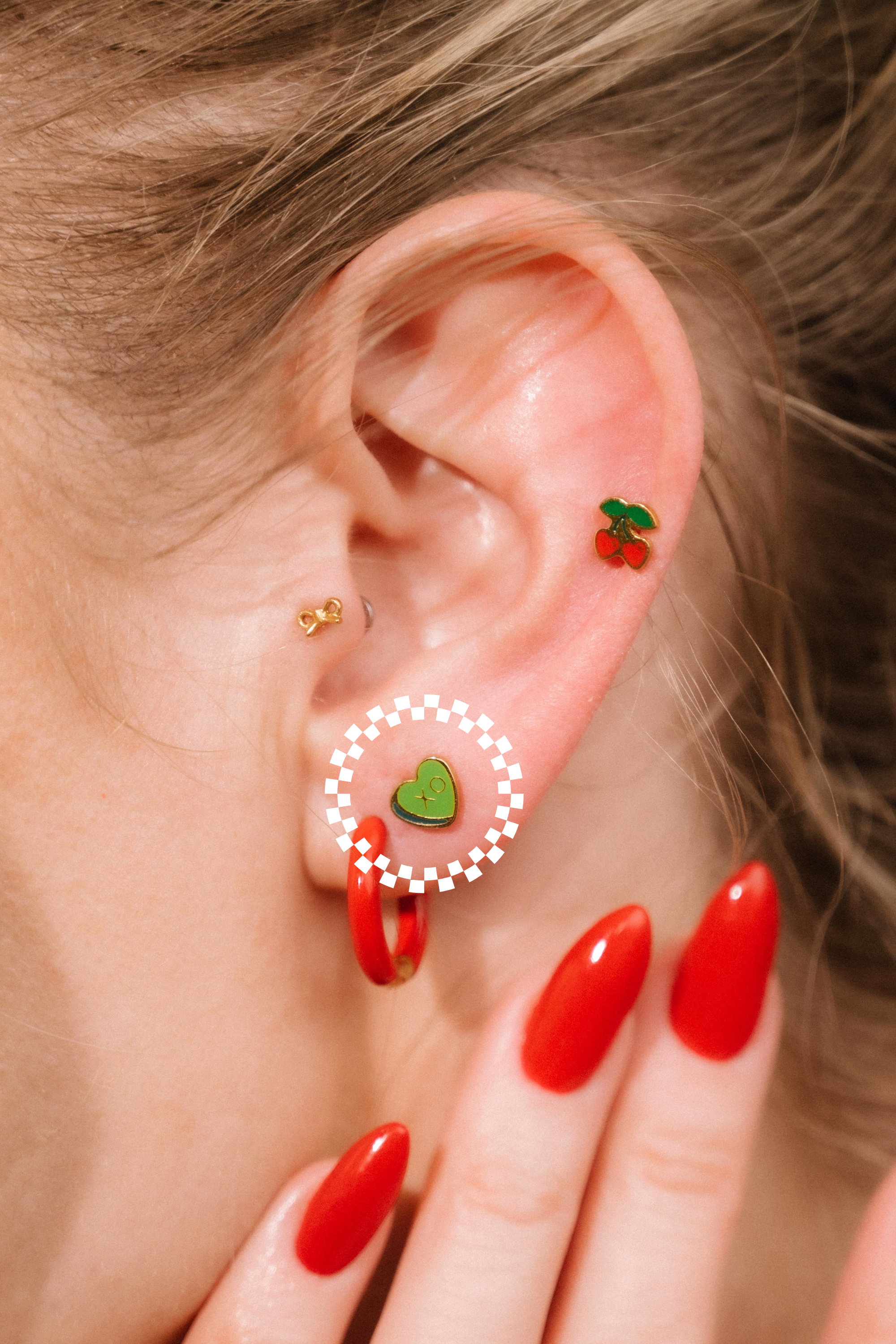 Close-up of an ear with colorful earrings and red nail polish.