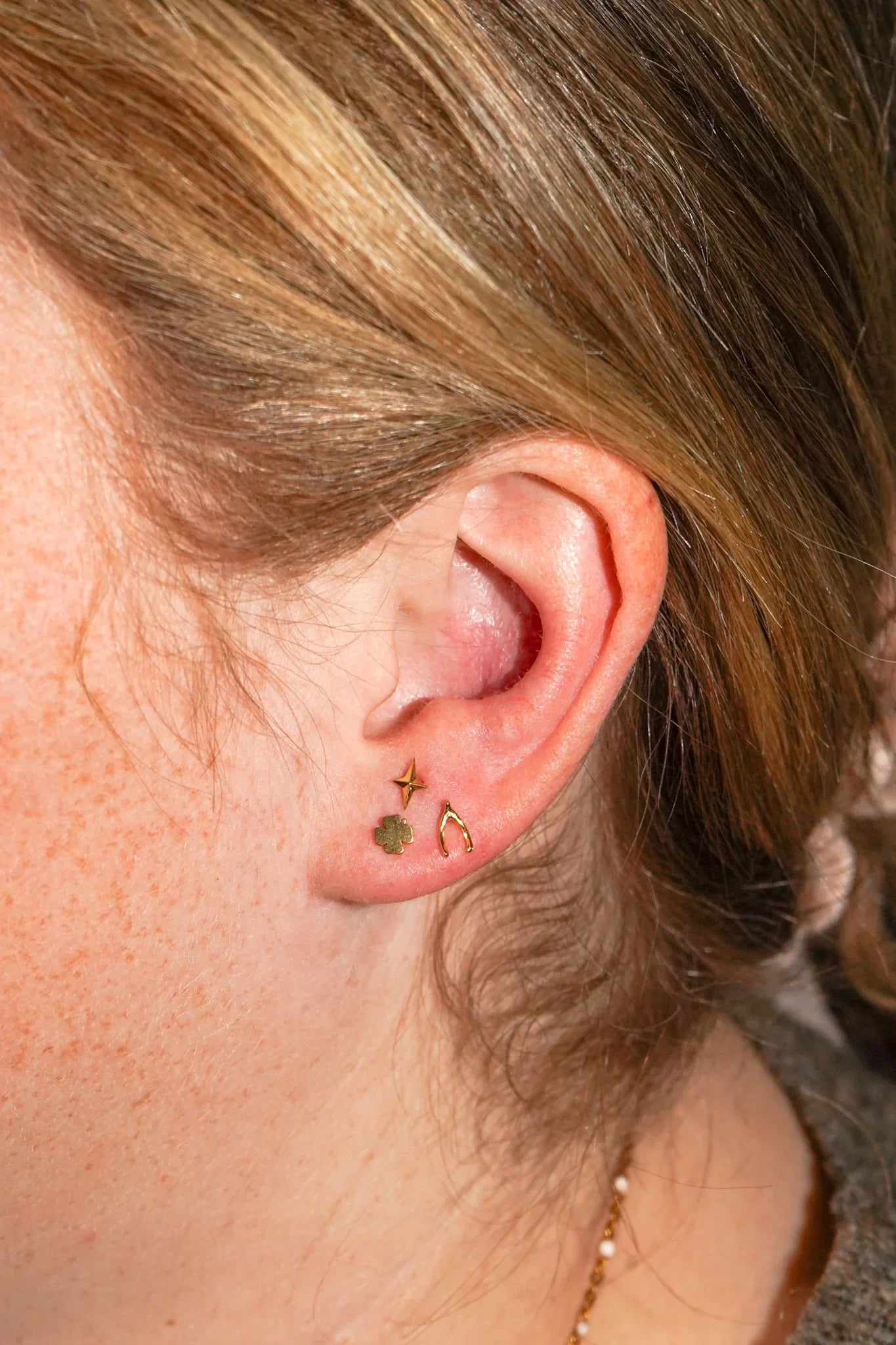 Close-up of an ear with a cluster of three different gold flat back studs on the lobe.