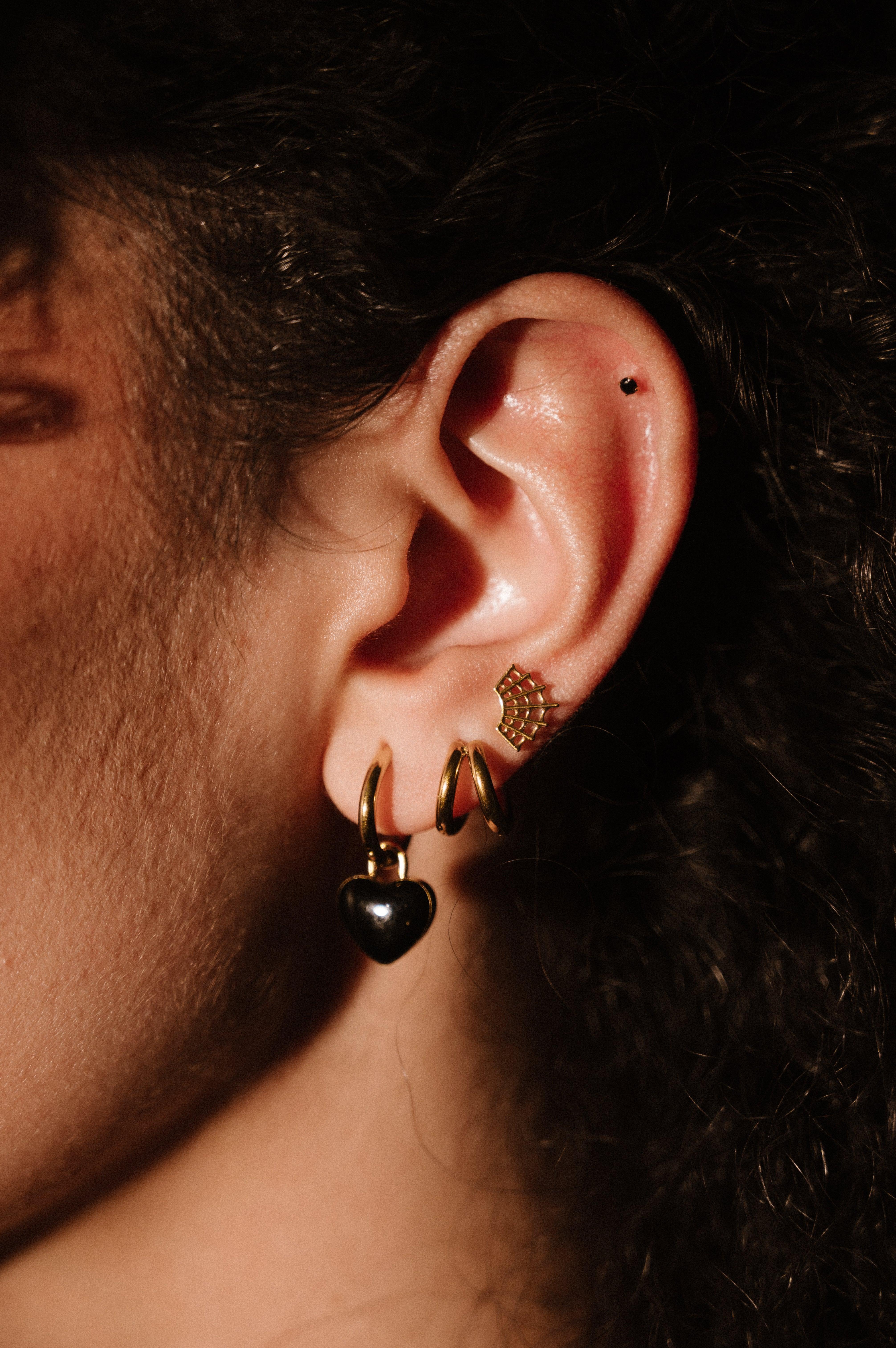 Close-up of an ear with gold and black earrings against a dark background