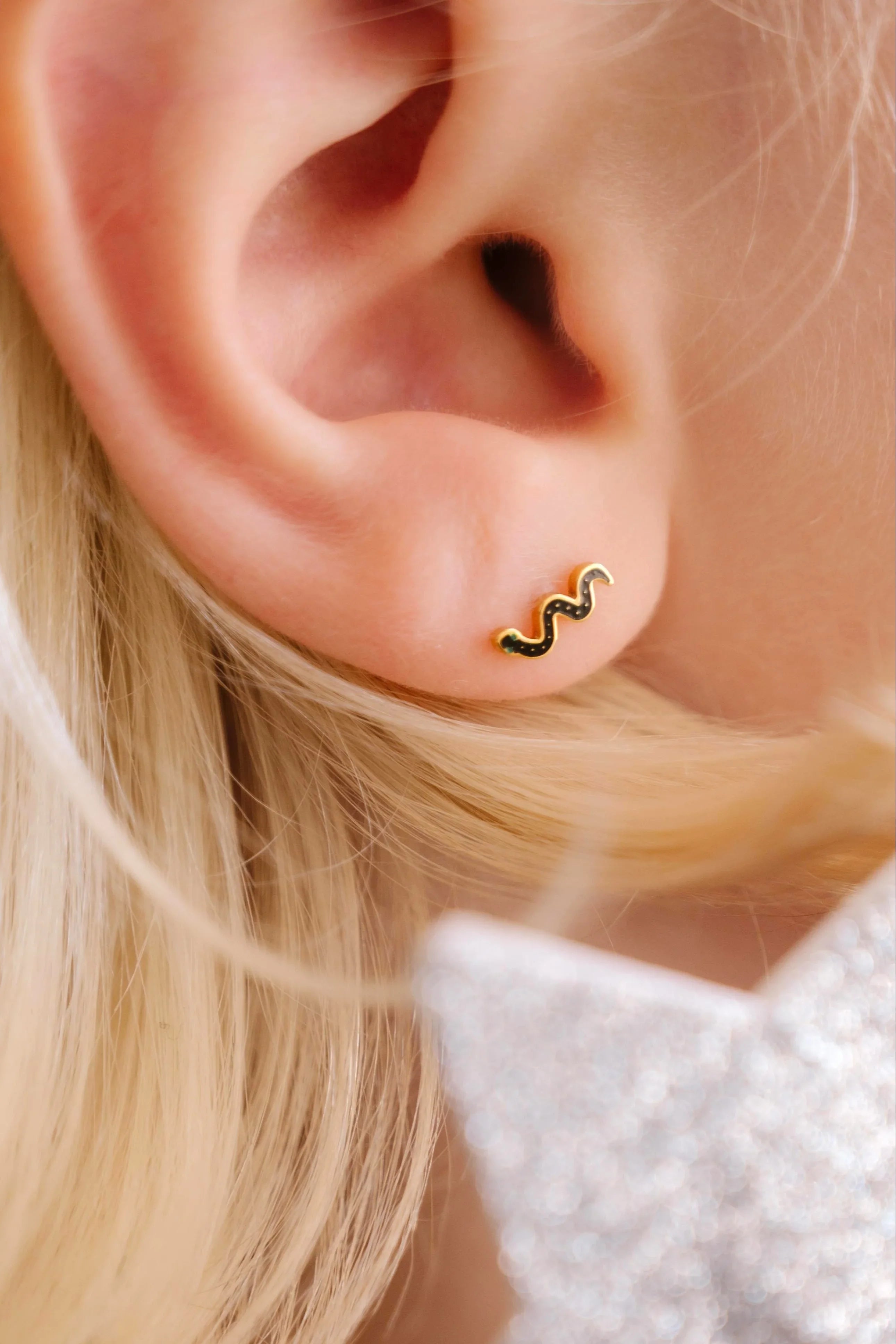 Close-up of a person wearing a gold and black snake earring with a blurred star-shaped object in the foreground.