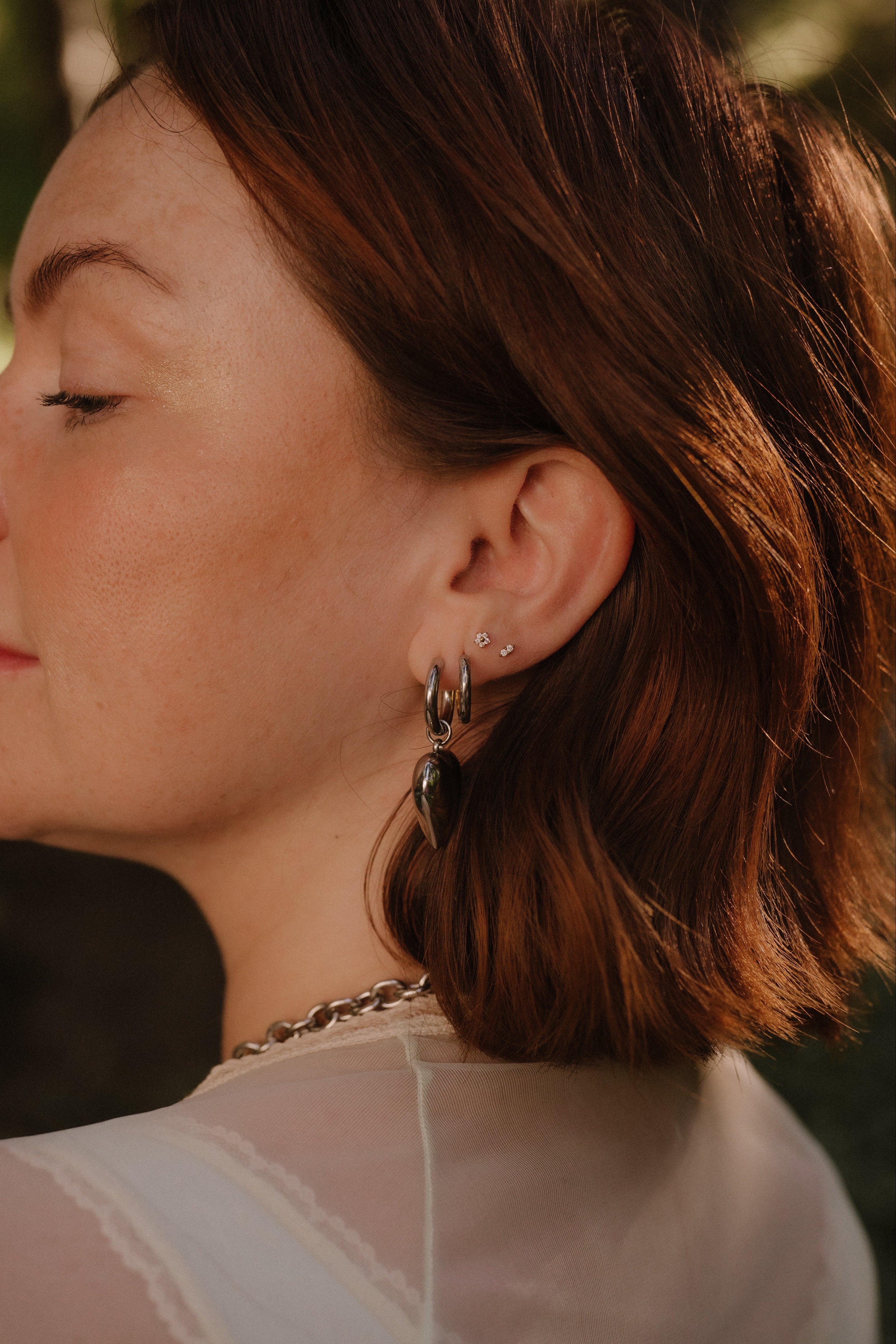 Close-up of a person wearing earrings with a blurred natural background