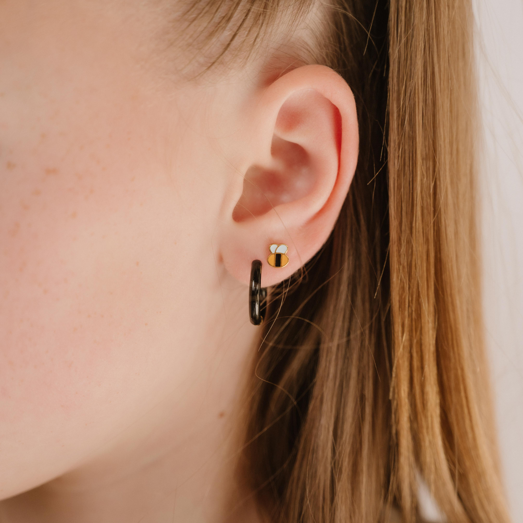 A close up of a bumblebee shaped flat back stud with yellow and black enamel and gold-plated titanium metal.