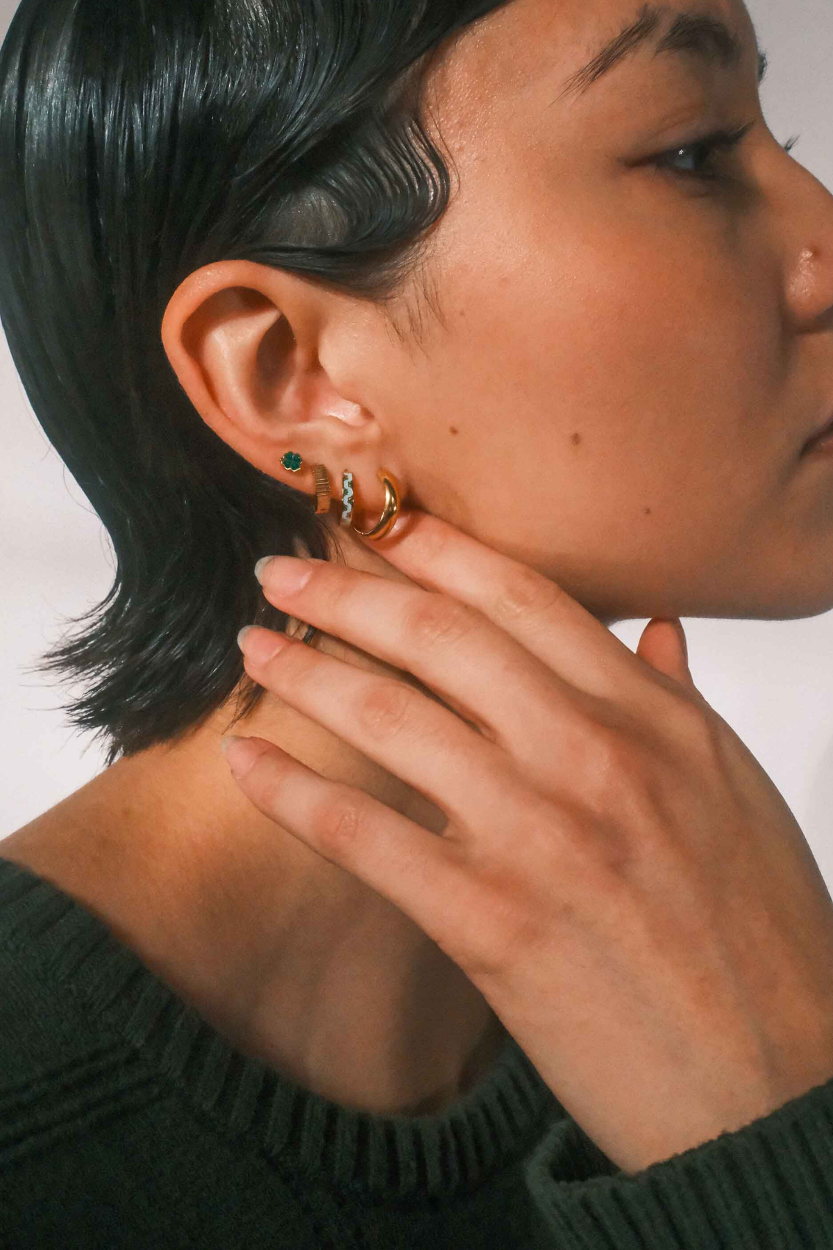 Close-up of a person wearing multiple earrings against of plain background