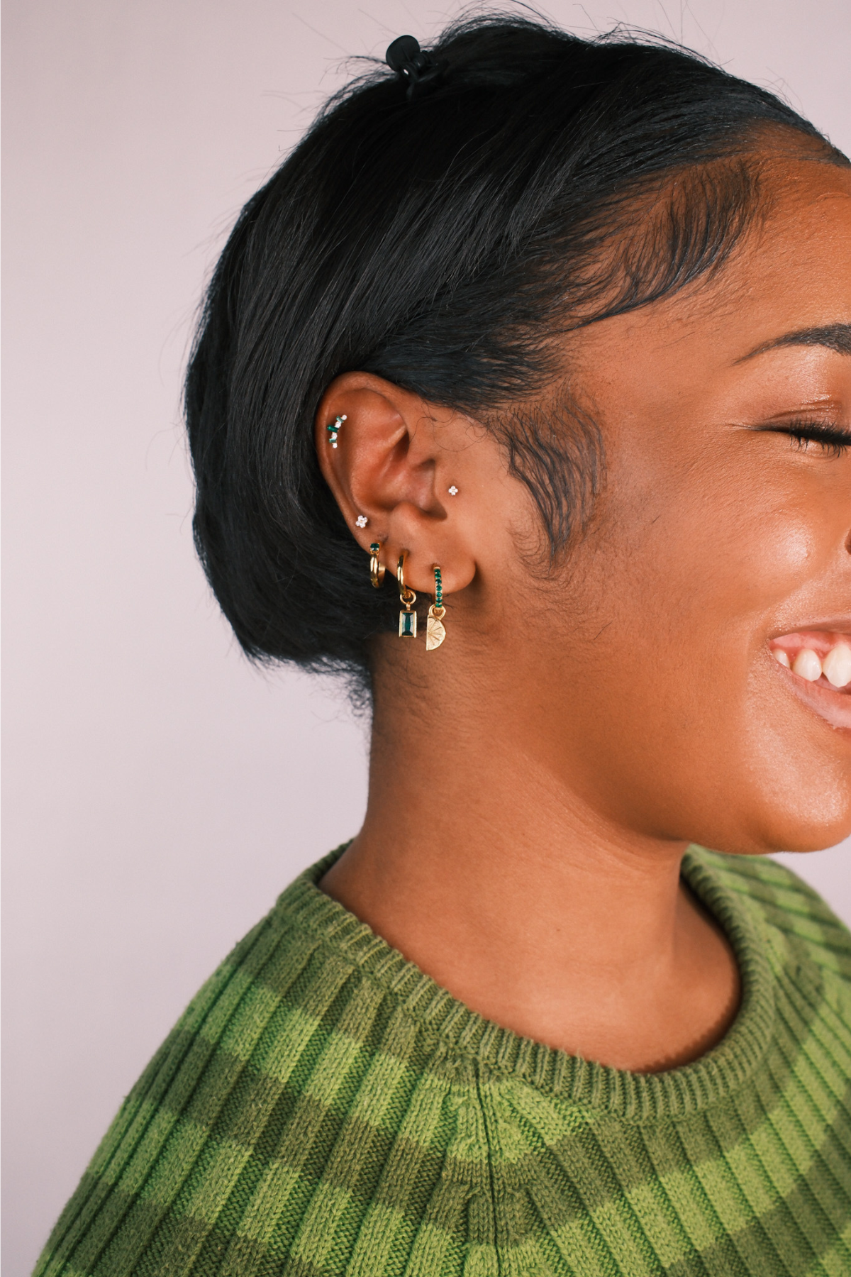 Close-up of a person wearing multiple earrings with a plain background