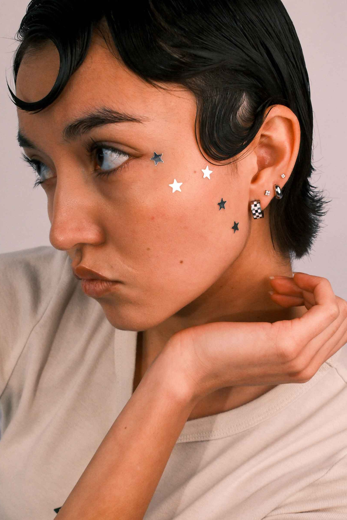 Close-up of a person wearing multiple earrings against a neutral background