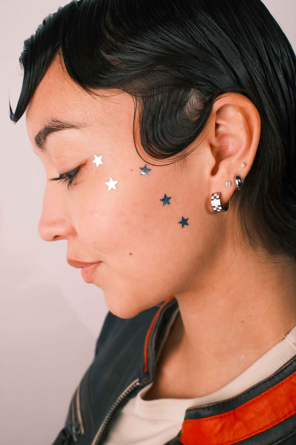 Close-up of a person wearing multiple earrings against a neutral background