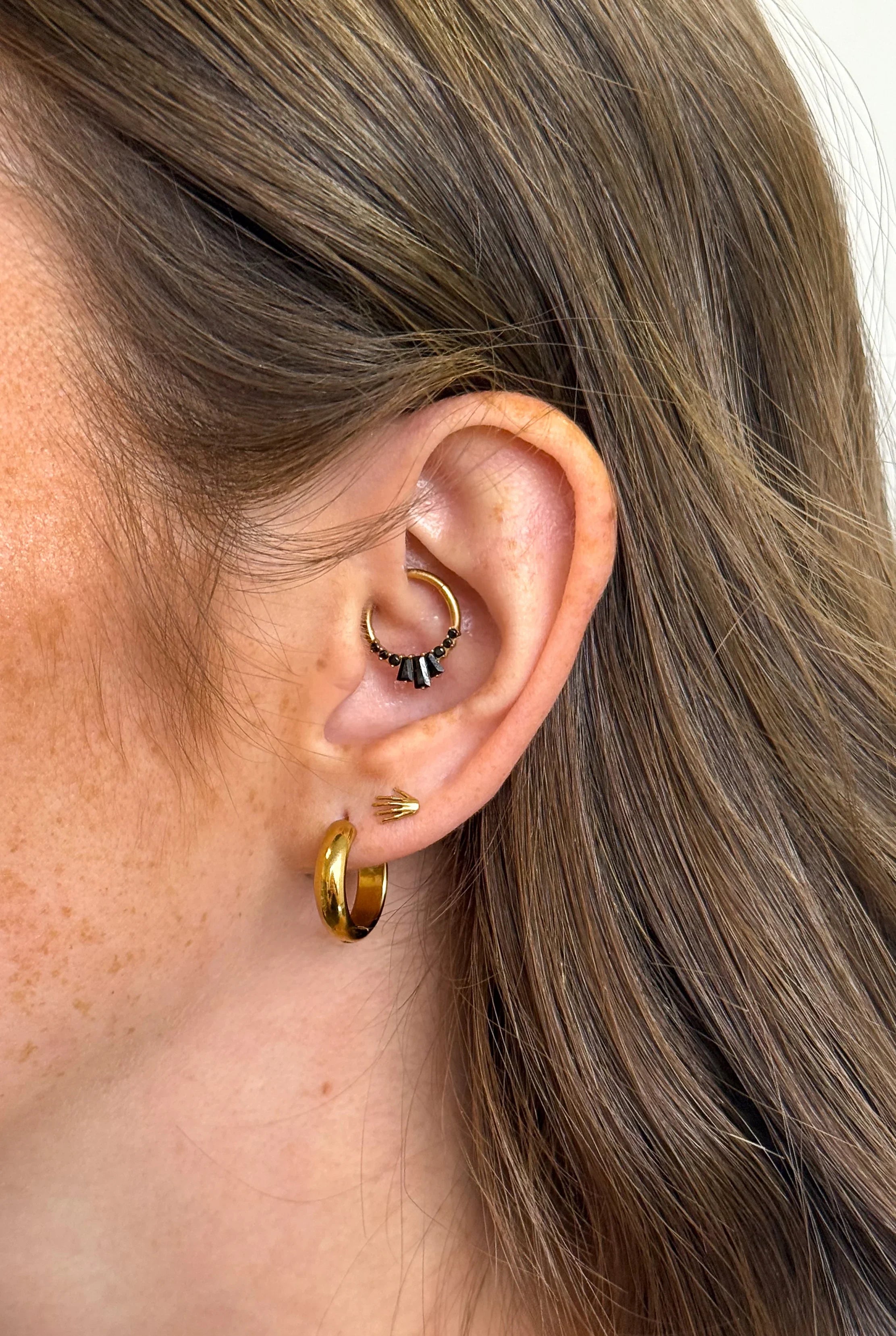 Close-up of an ear wearing gold hoops and stud earrings with a neutral background