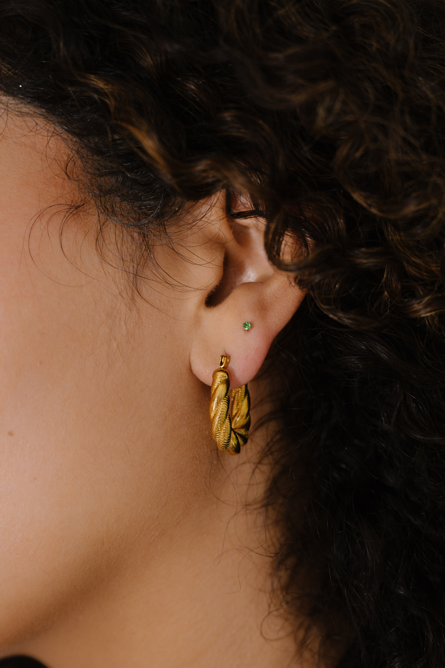 Close-up of a person wearing a gold earring with a blurred background