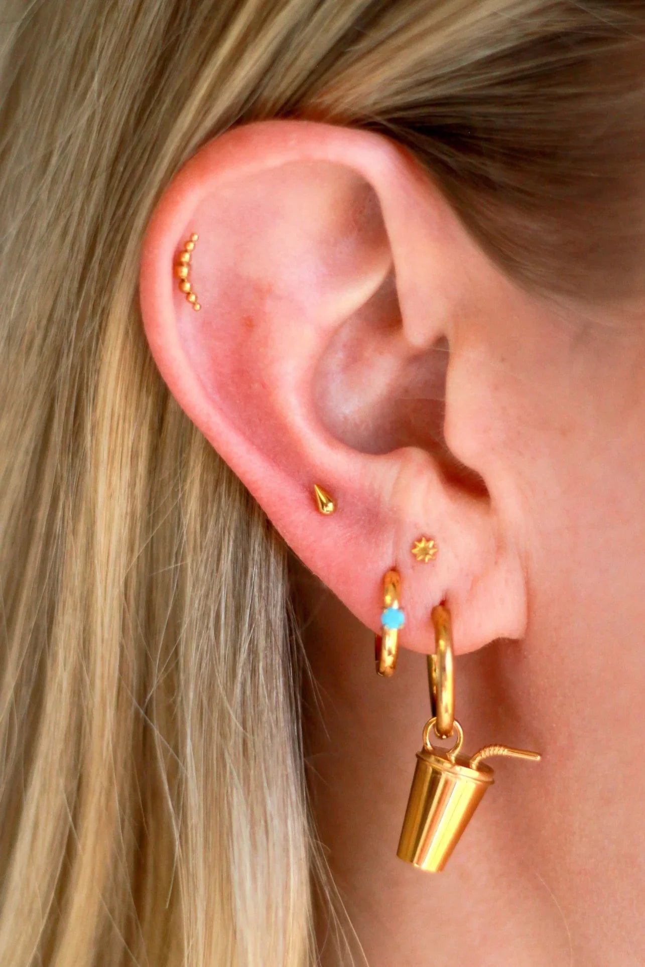 Close up of an ear with a lot of piercings, featuring gold flat backs studs and hoops