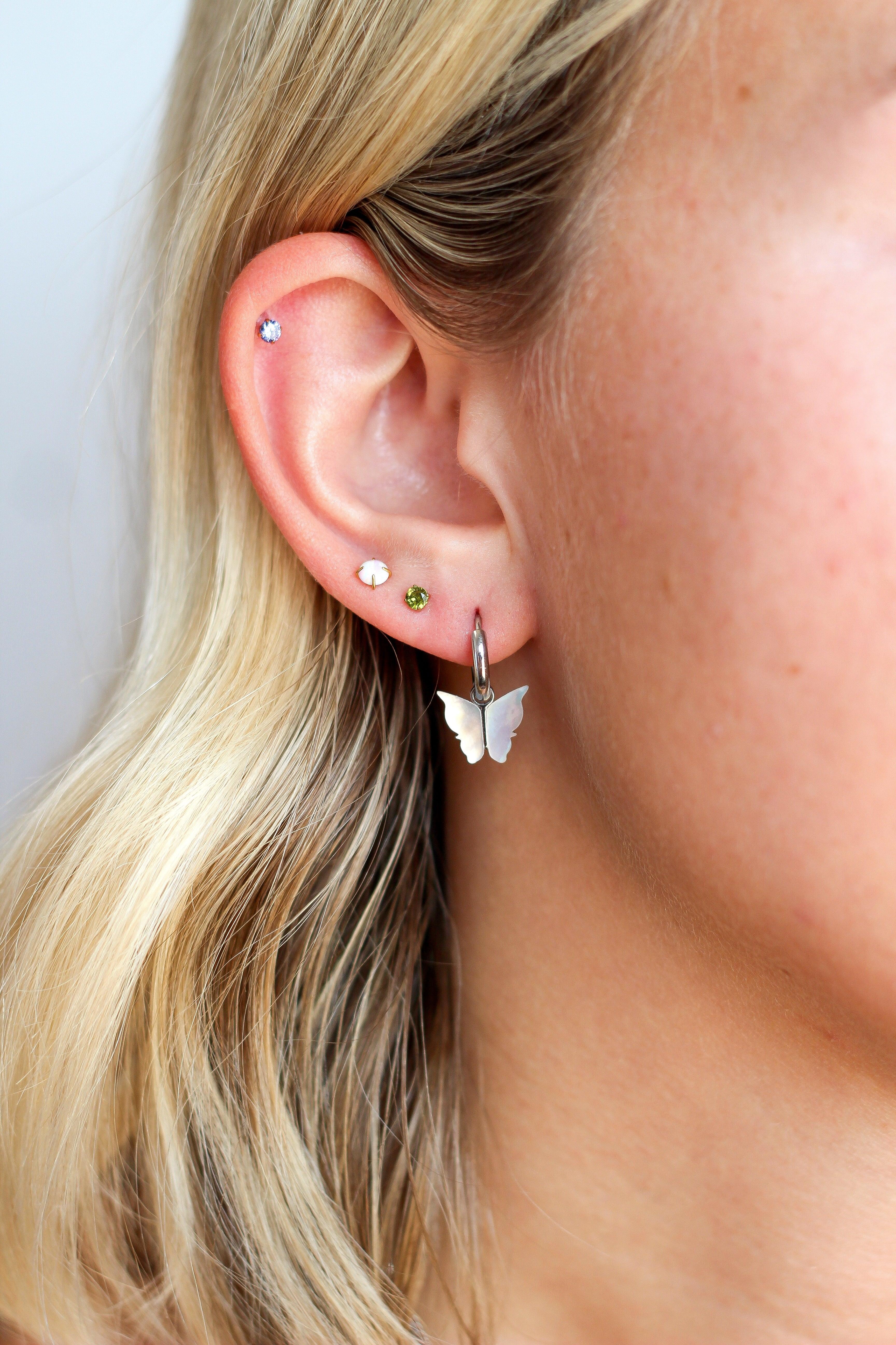 Close-up of a person wearing butterfly-shaped earrings with a plain background