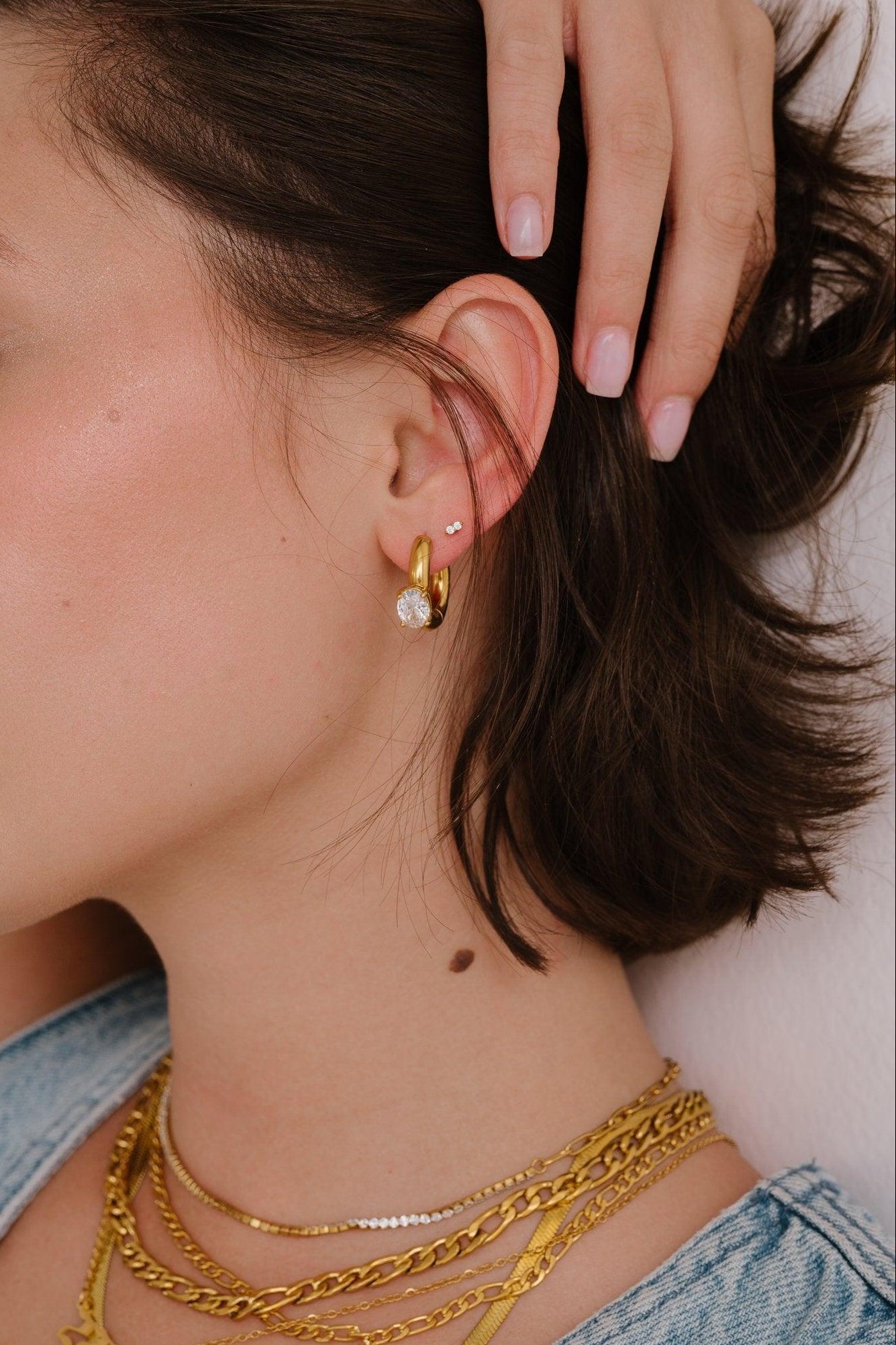 Woman wearing gold necklaces and earrings with a close-up of her ear.