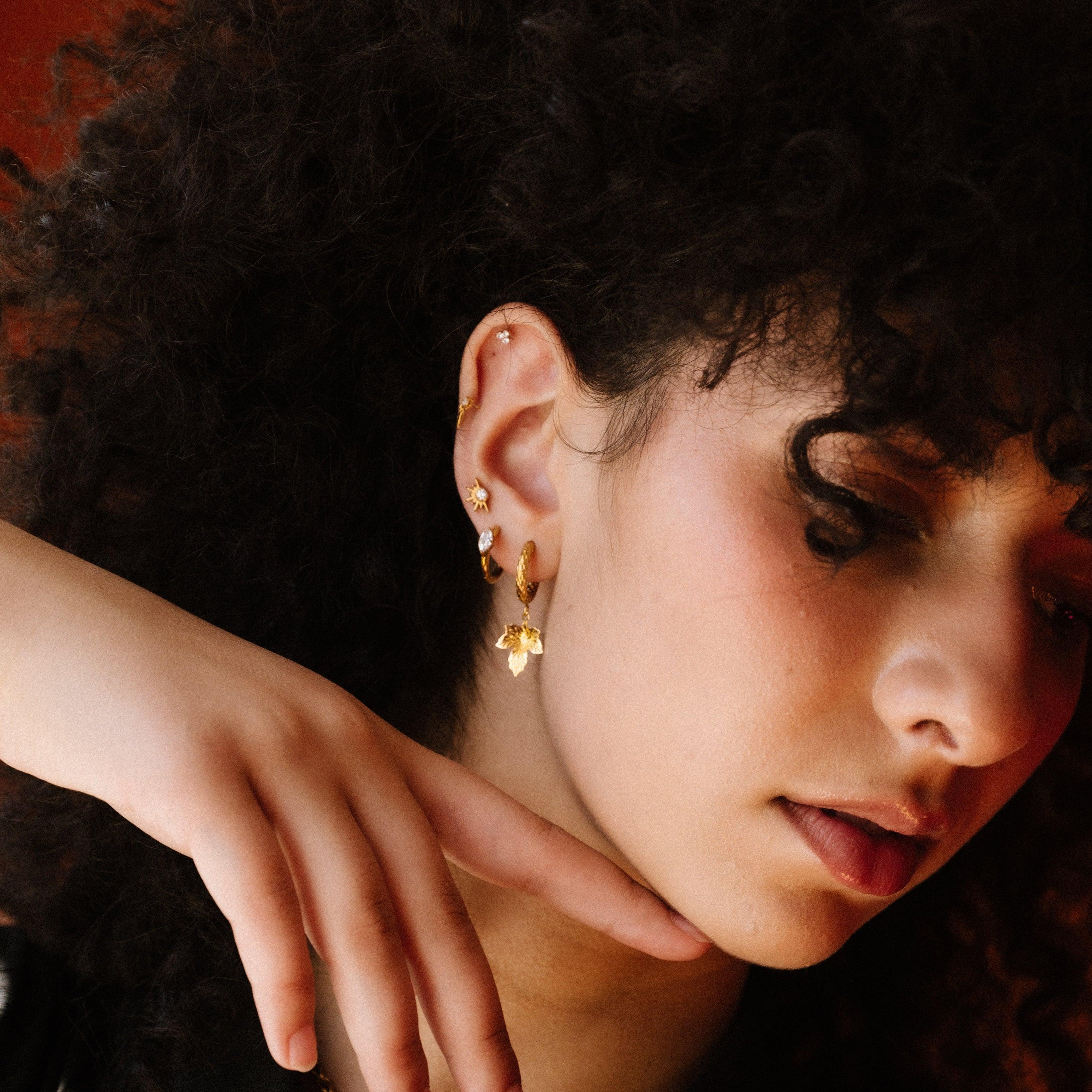 Woman with curly hair wearing gold earrings against an orange background