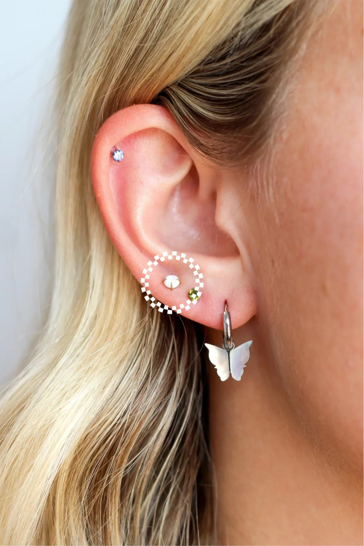 Close-up of a person wearing a butterfly earring with several colorful studs a blurred background