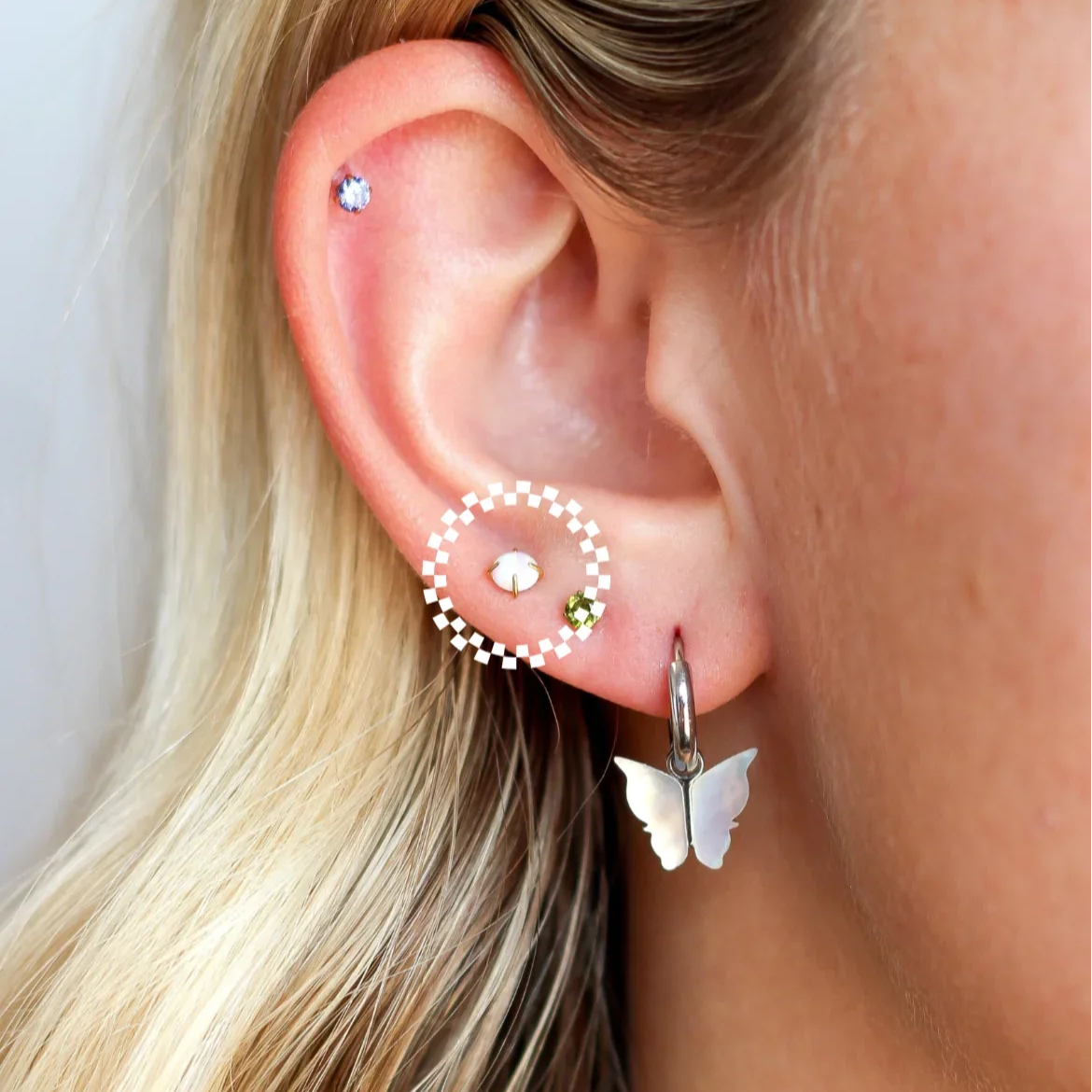 Close-up of a person wearing a butterfly earring with several colorful studs a blurred background