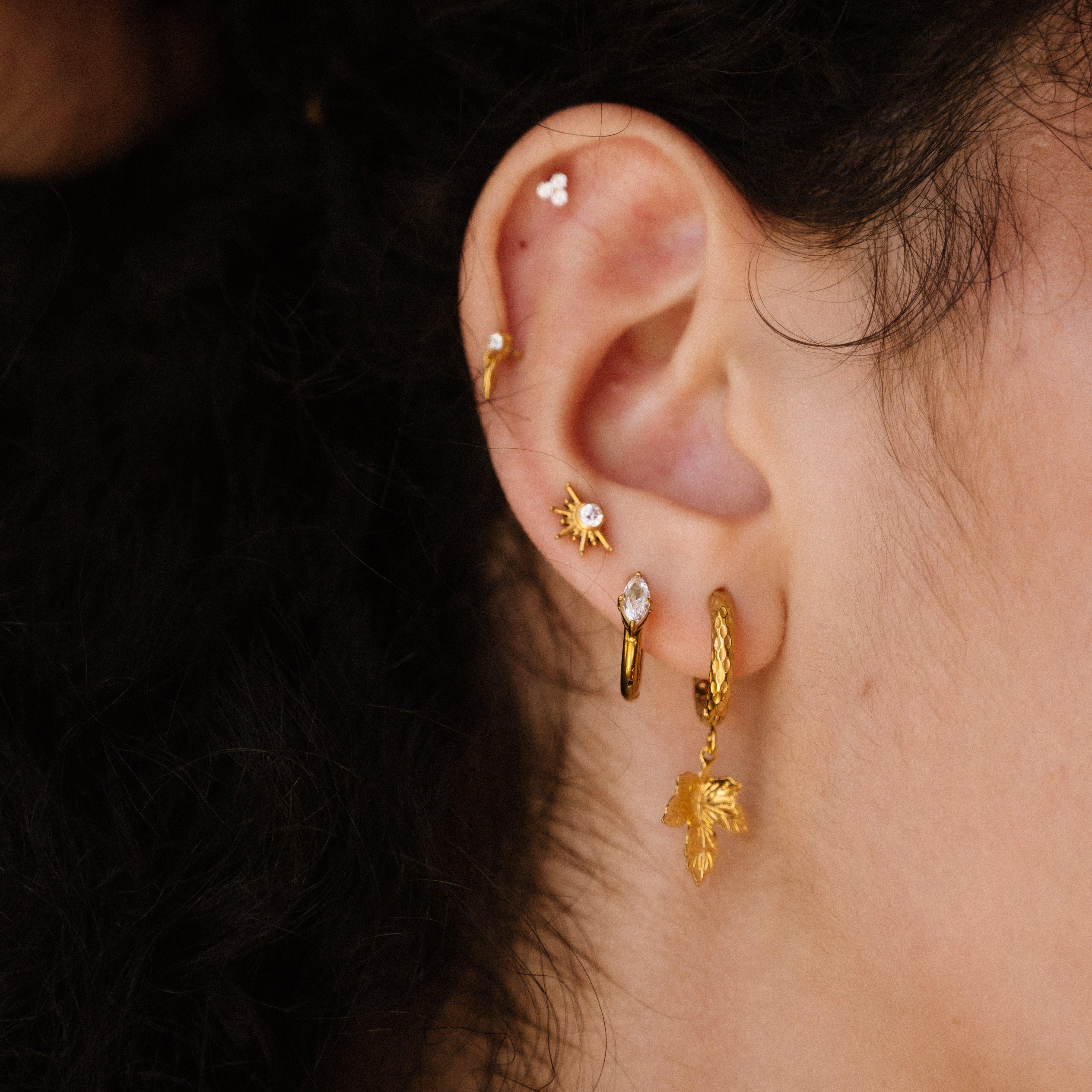 Close-up of an ear with gold earrings against a blurred background
