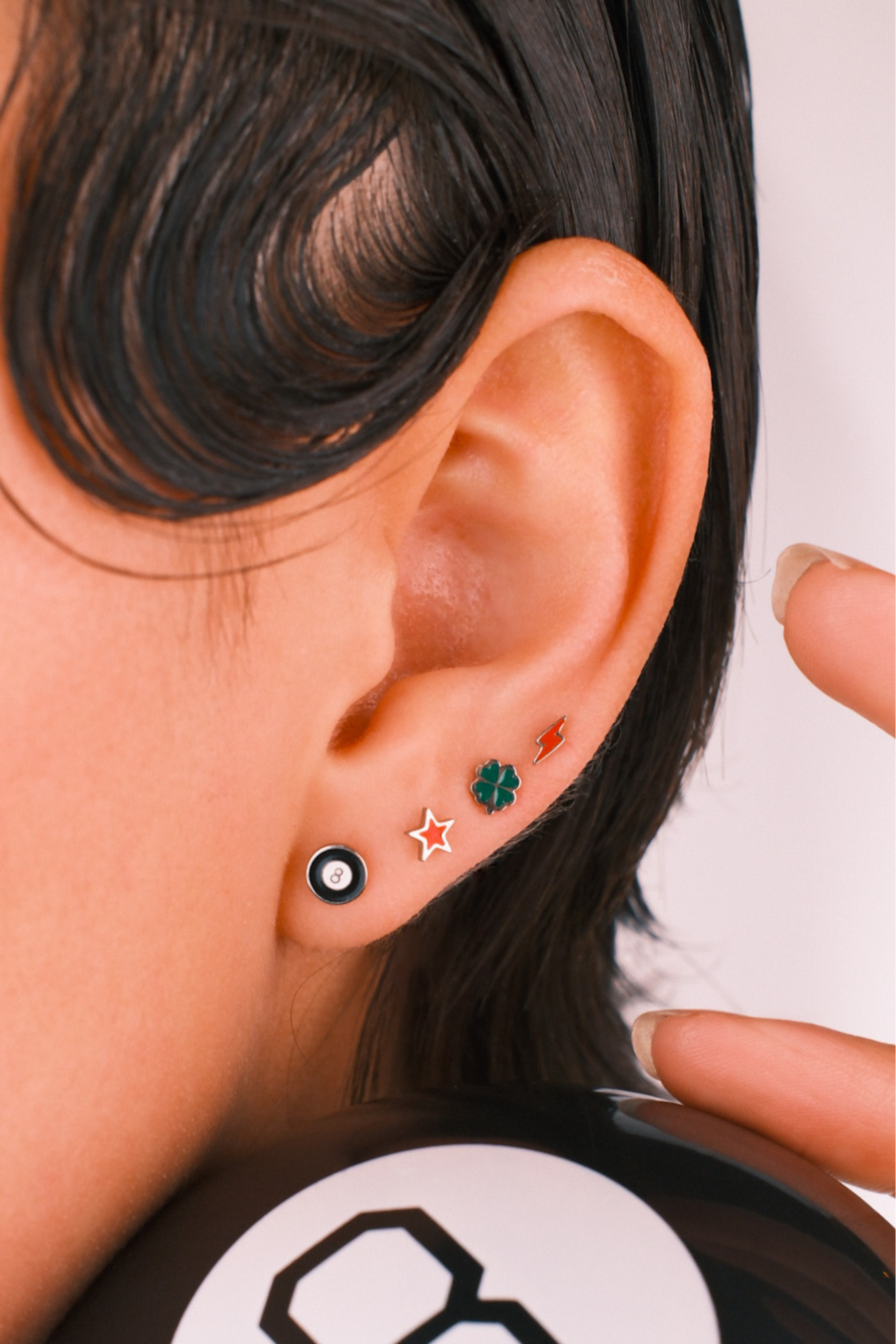 Close-up of an ear wearing four flat back stud enamel earrings with a blurred background