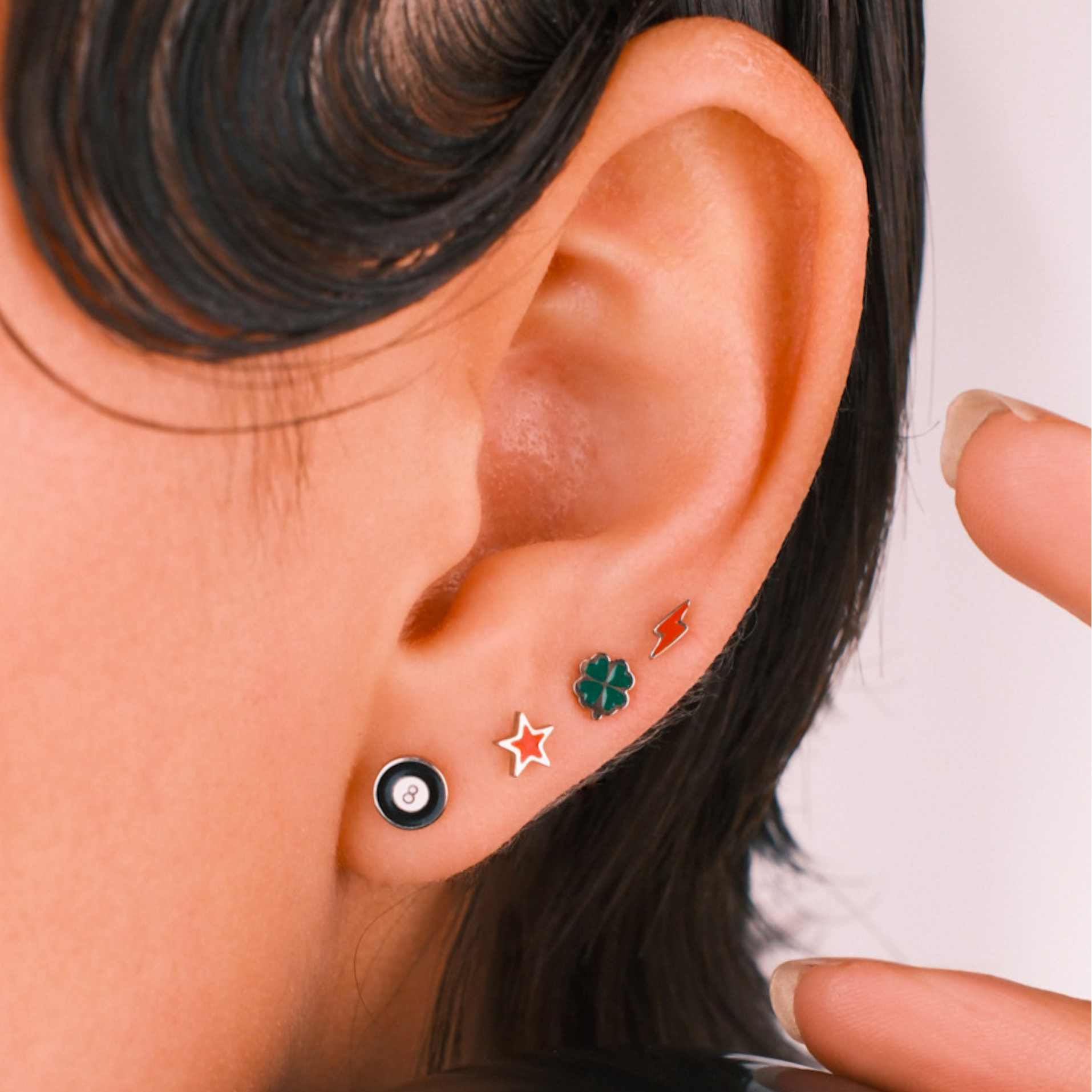Close-up of an ear wearing four flat back stud enamel earrings with a blurred background
