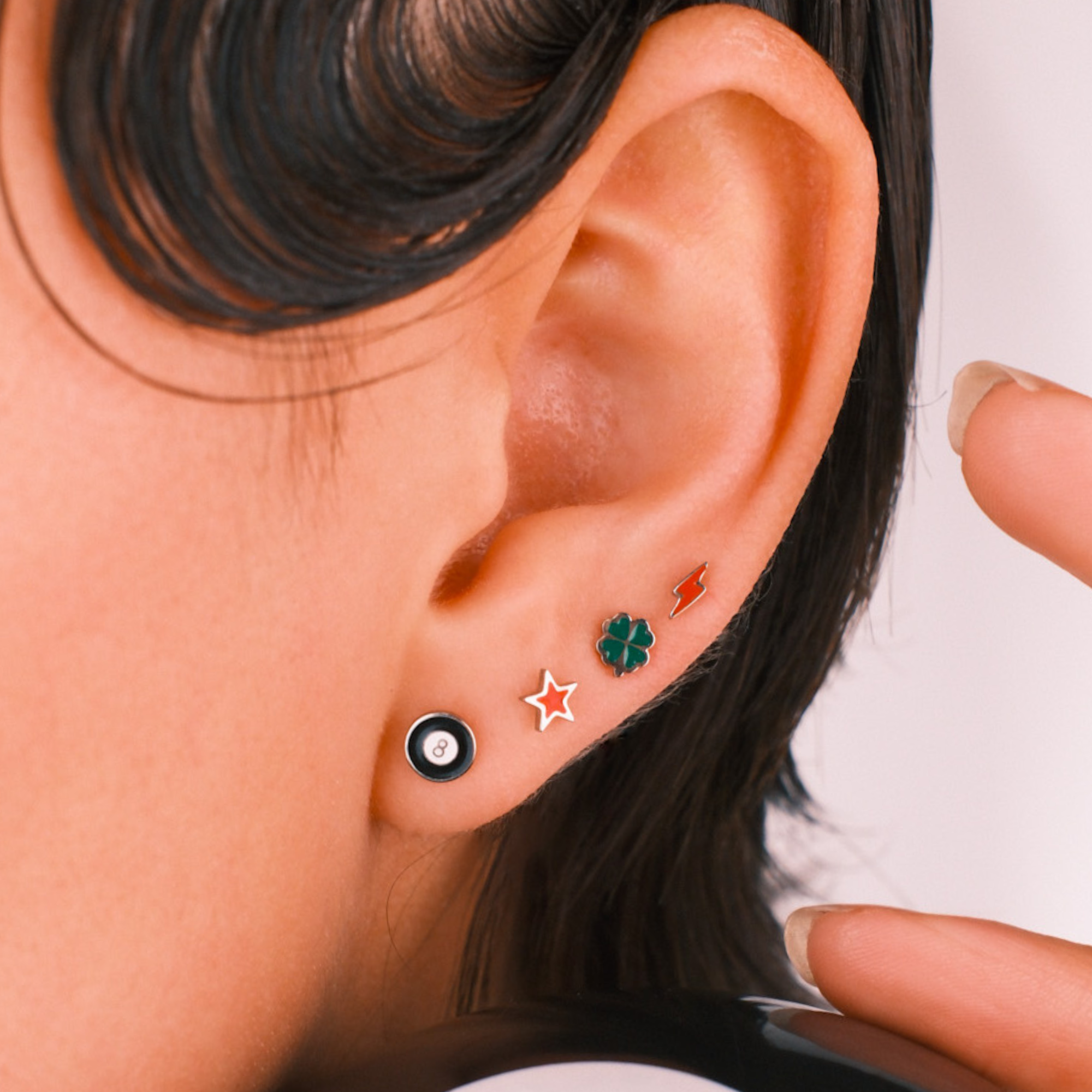 Photo of a person wearing multiple flat back stud earrings, including 1 in the shape of an 8 ball in black and white