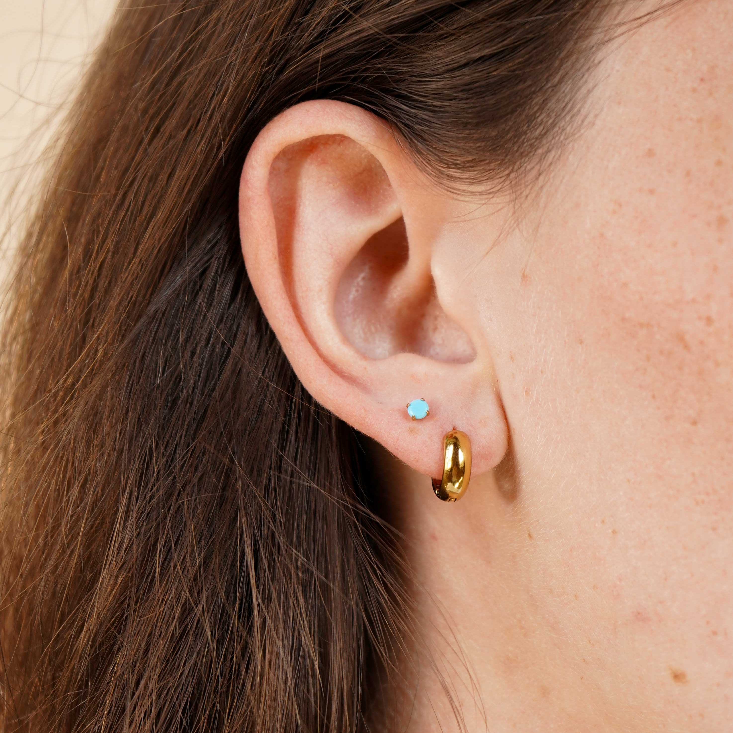 Close-up of an ear with gold hoop earrings and a blue gemstone earring.