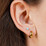 Close-up of an ear wearing a gold hoop earring and a small blue gemstone earring.