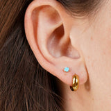 Close-up of an ear wearing a gold hoop earring and a small blue gemstone earring.