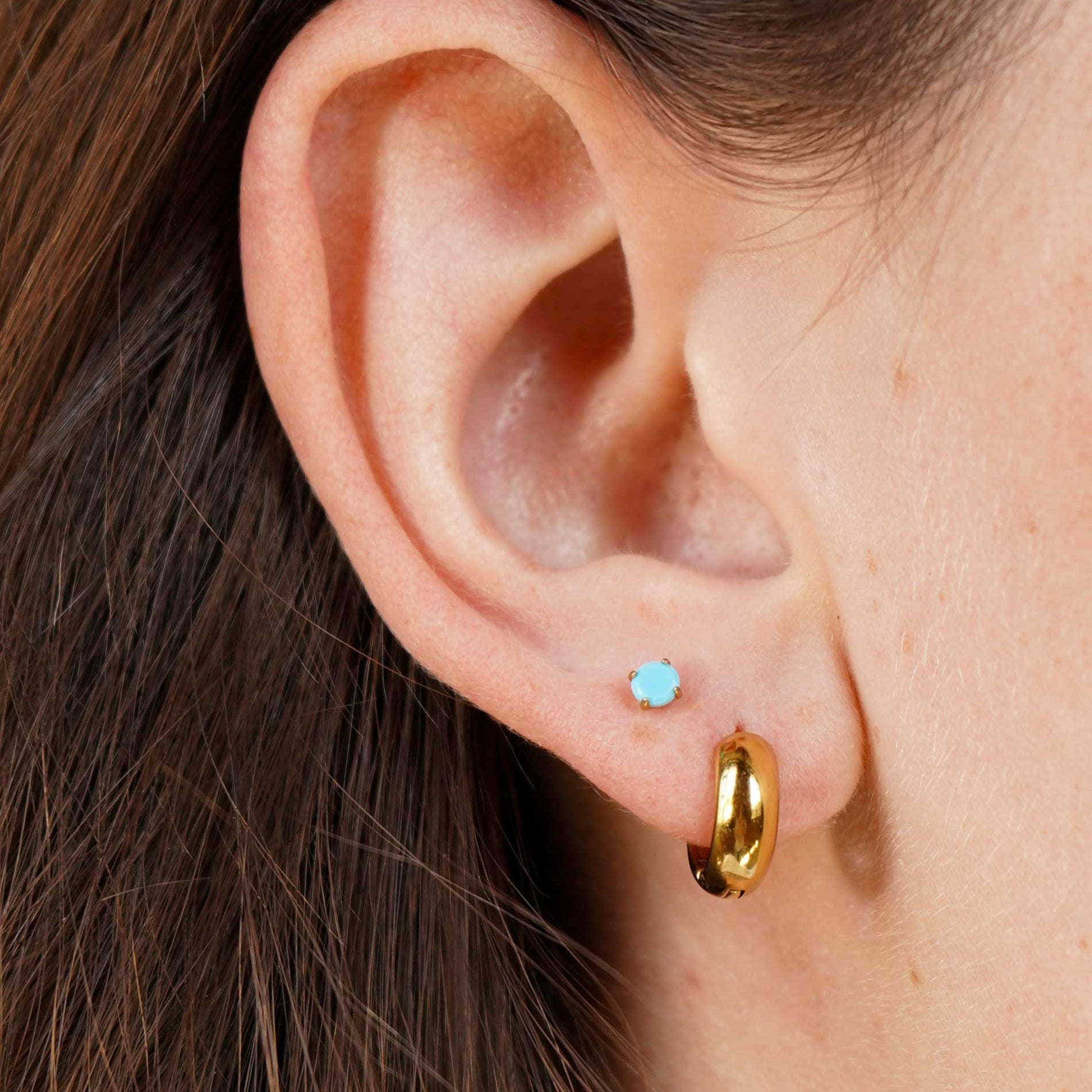 Close-up of an ear wearing a gold hoop earring and a small blue gemstone earring.