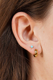 Close-up of an ear wearing a gold hoop earring and a small blue gemstone earring.