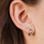 Close-up of an ear with two earrings: a small blue stud and a larger silver hoop.