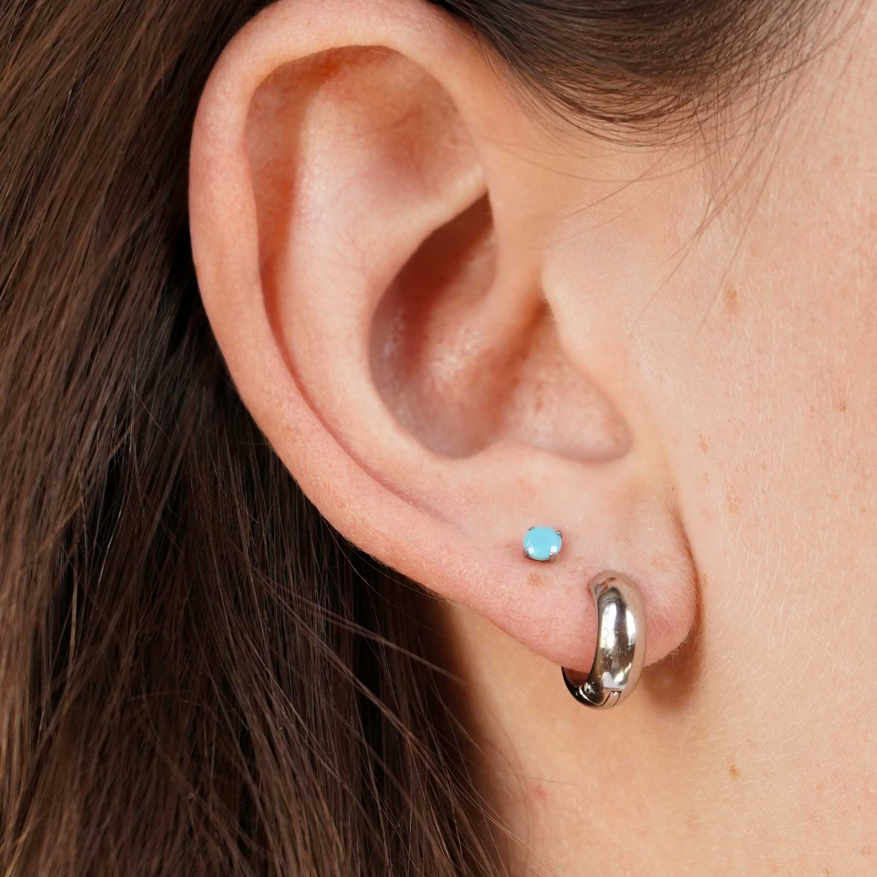 Close-up of an ear with two earrings: a small blue stud and a larger silver hoop.