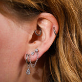 Close up of  a model wearing multiple earrings, including a clicker-style hoop featuring a bubble-like metal pattern on the bottom 3/4 of the hoop in the Daith piercing. Made from ASTM F136 Implant-Grade Titanium