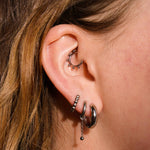 Close up of a model wearing multiple earrings, including clicker-style hoop featuring a series of round metal details that radiate from the main hoop in the Daith piercing. Made from ASTM F136 Implant-Grade Titanium