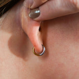 A close up of a model's ear wearing a hoop earring that features a split design where one half of the hoop is silver in color and the other is gold. Hoops are made from ASTM F136 Implant Grade Titanium and the gold half is finished with 18k Gold PVD plating.