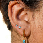 Close-up of an ear with gold hoop earrings and faux turquoise gemstones.