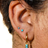 Close-up of an ear with gold hoop earrings and faux turquoise gemstones.