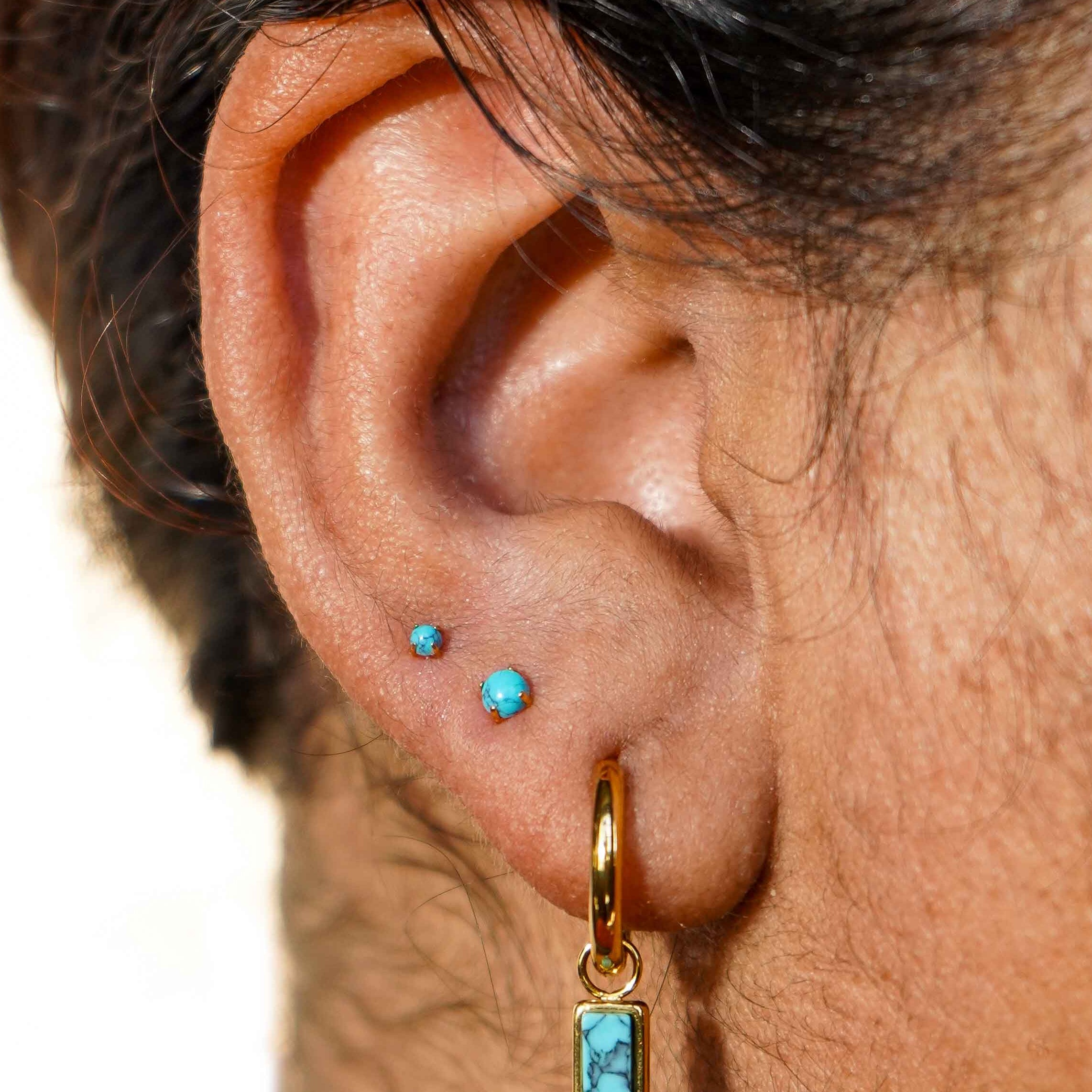 Close-up of an ear with gold hoop earrings and faux turquoise gemstones.