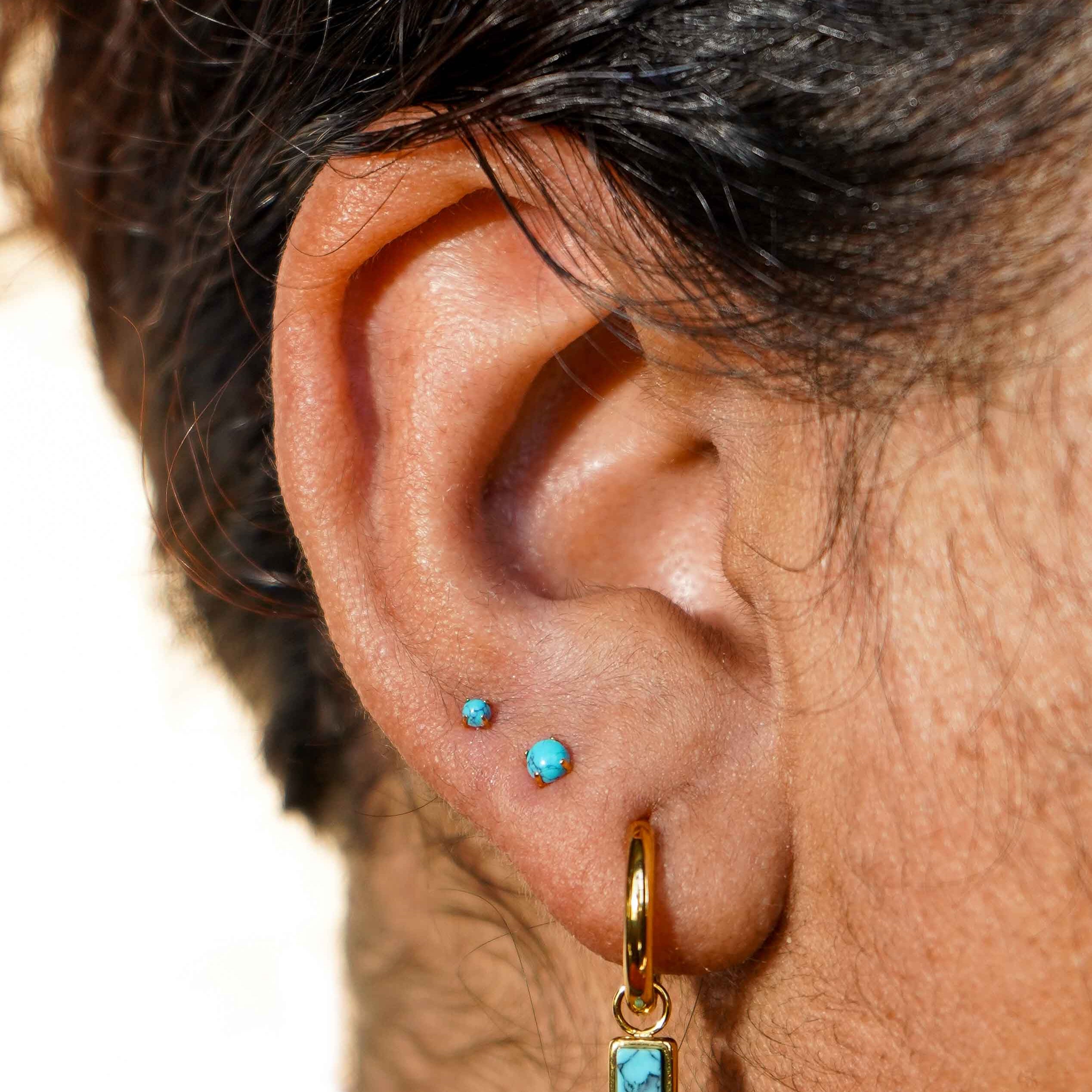 Close-up of an ear with gold hoop earrings and faux turquoise gemstones.