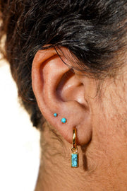 Close-up of an ear with gold hoop earrings and faux turquoise gemstones.