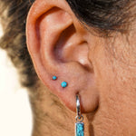 Close-up of an ear with a faux turquoise stone earring on a neutral background