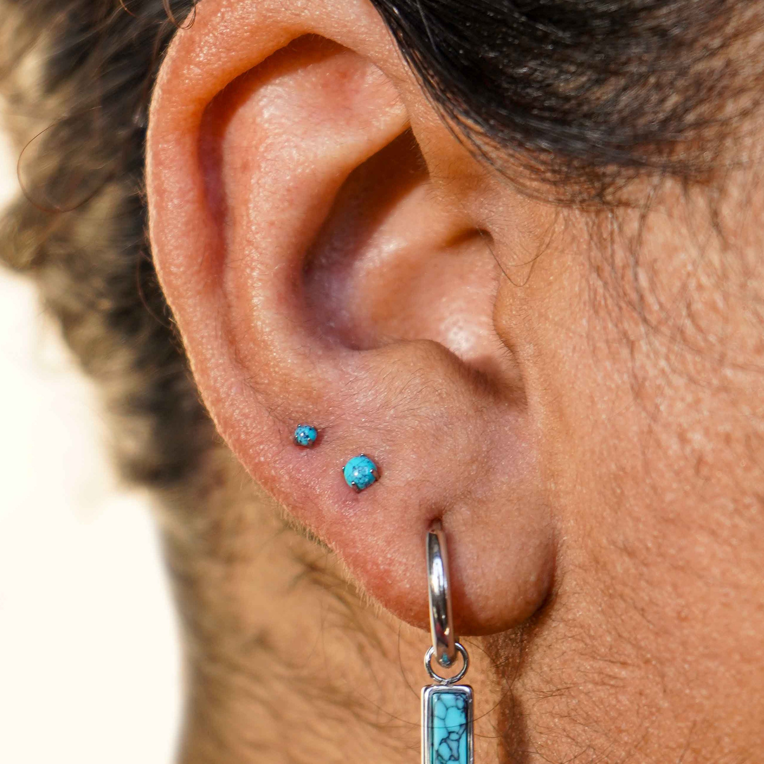 Close-up of an ear with a faux turquoise stone earring on a neutral background