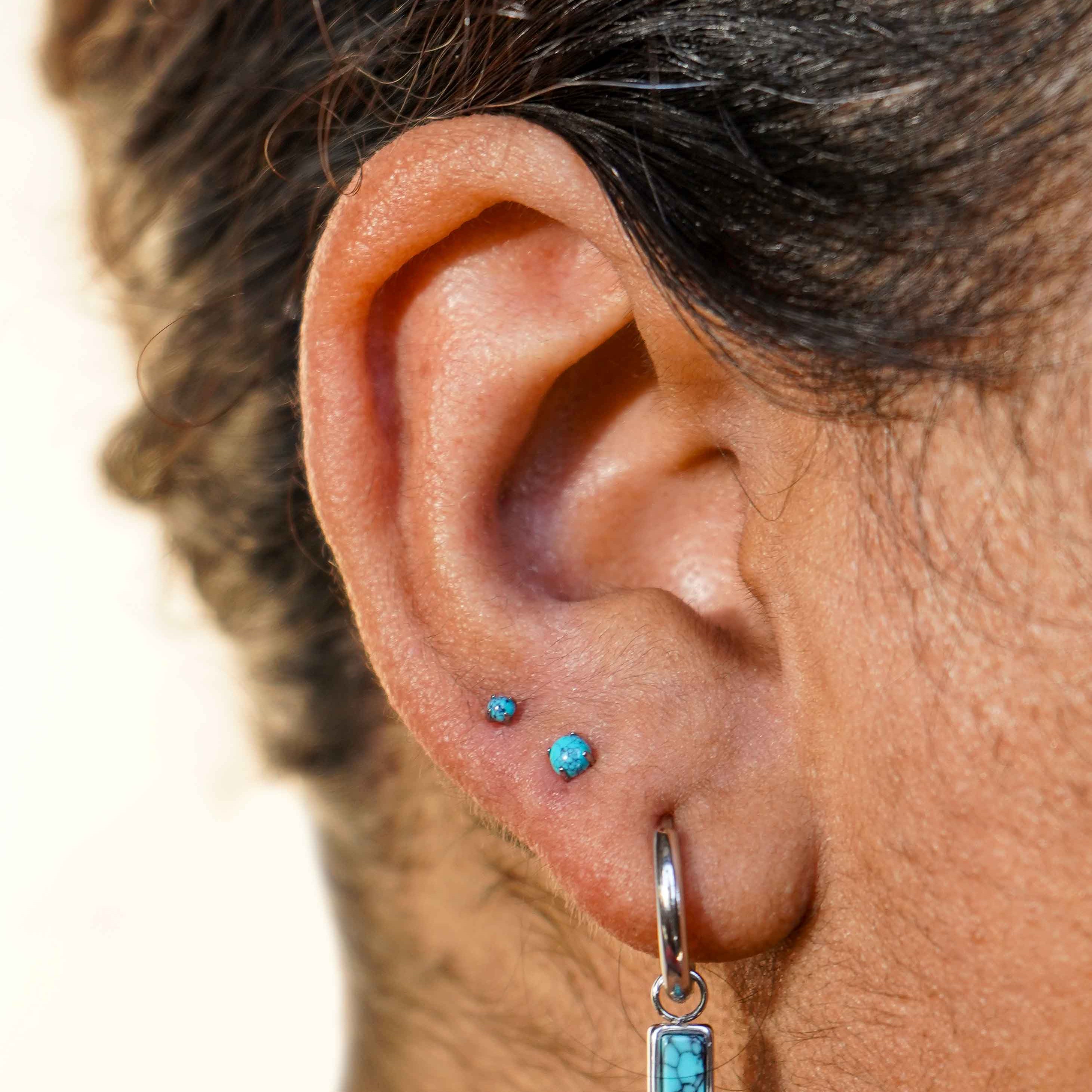 Close-up of an ear with faux turquoise stone earrings on a neutral background