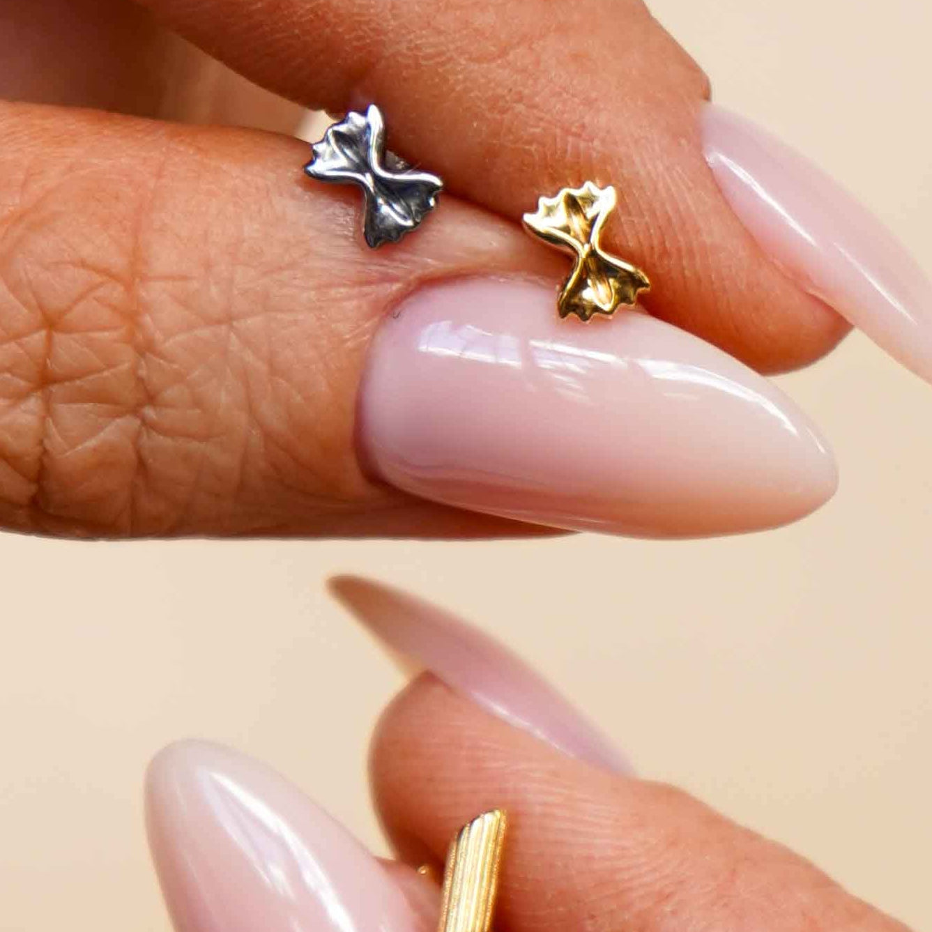 Close-up of a hand holding multiple gold and silver flat back stud earrings that are shaped like different pasta noodles.