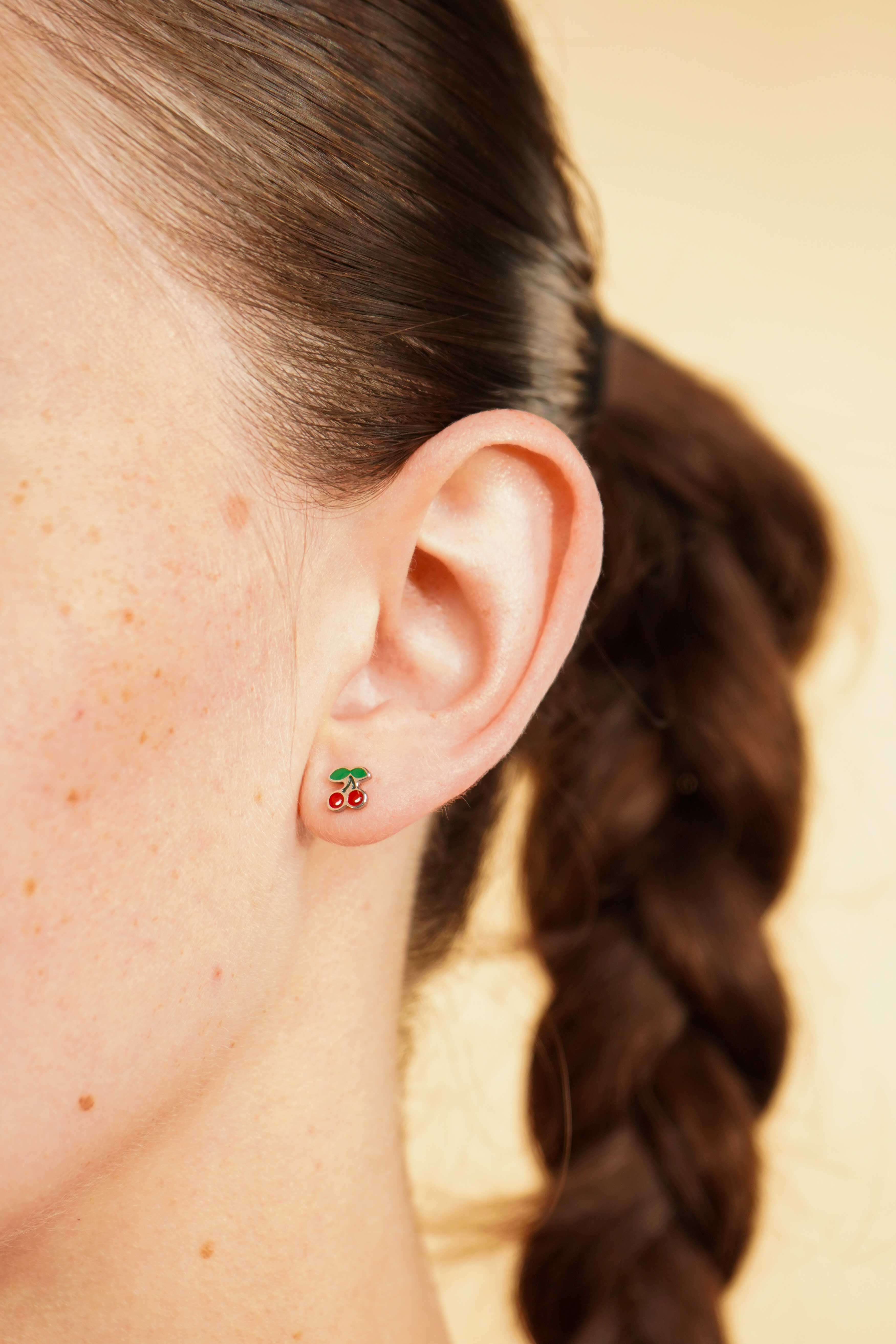 Close-up of an ear wearing a colorful enamel and titanium silver double cherry flat back stud earring with a blurred background