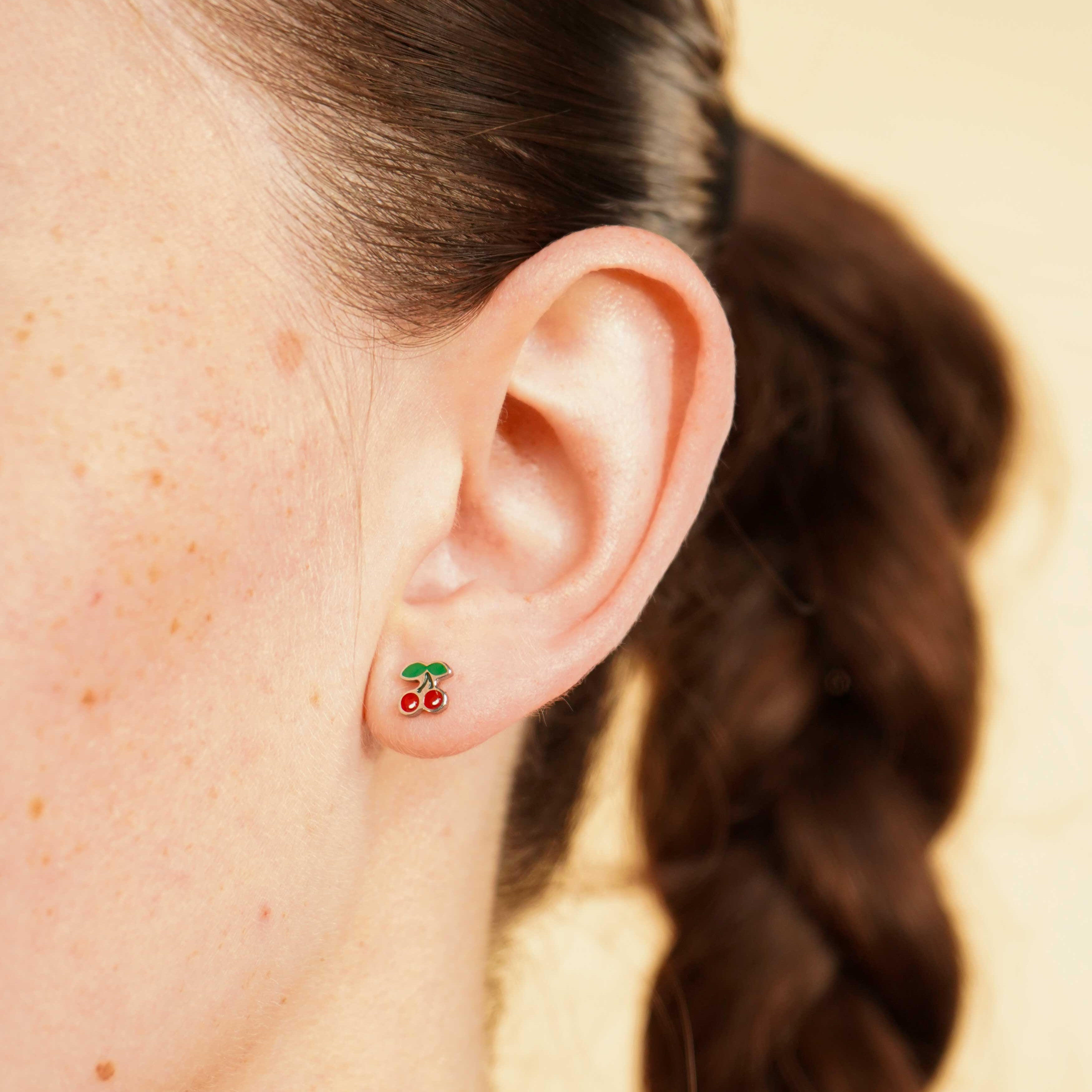 Close-up of an ear wearing a colorful enamel and titanium silver double cherry flat back stud earring with a blurred background