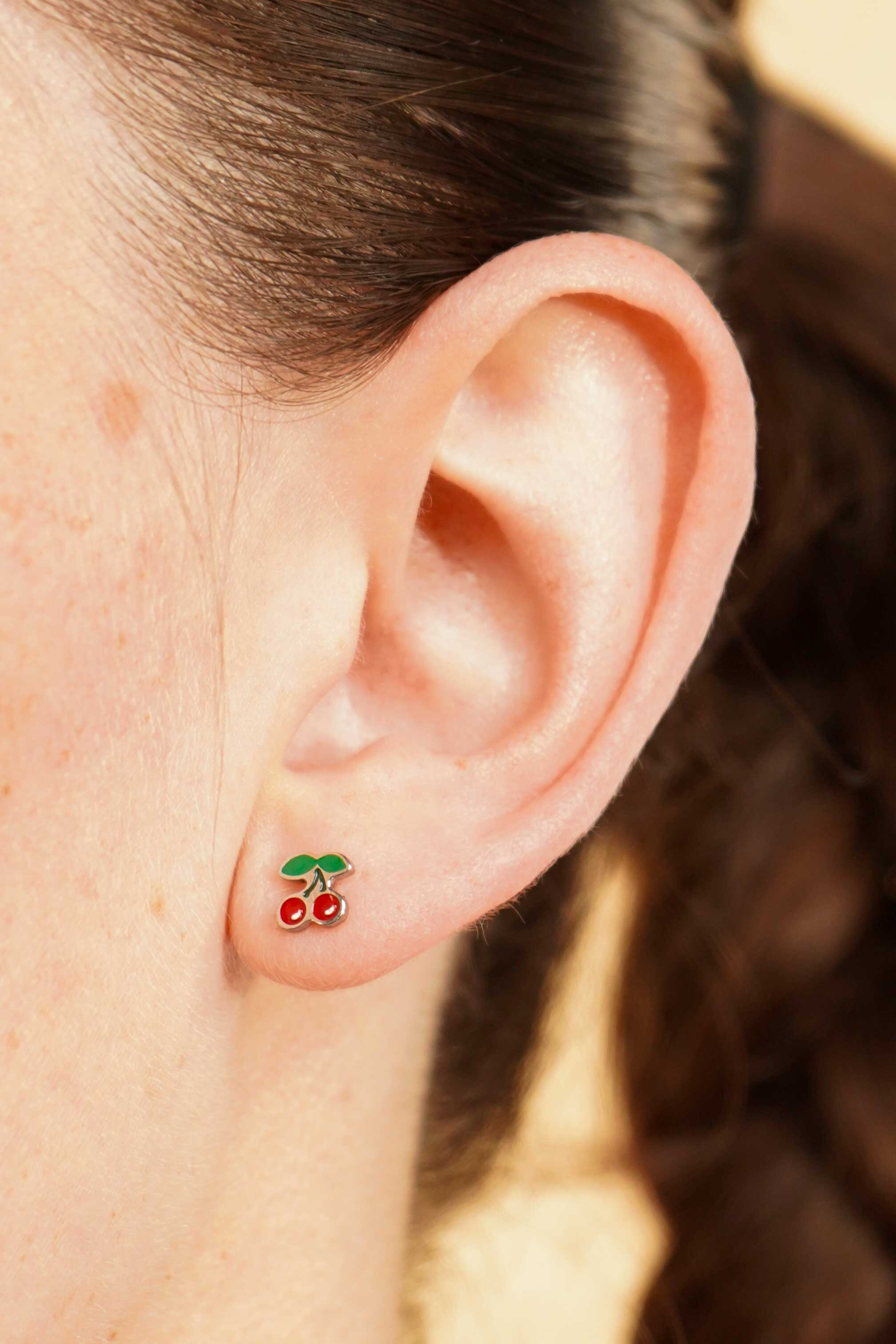 Close-up of an ear wearing a colorful enamel and titanium silver double cherry flat back stud earring with a blurred background