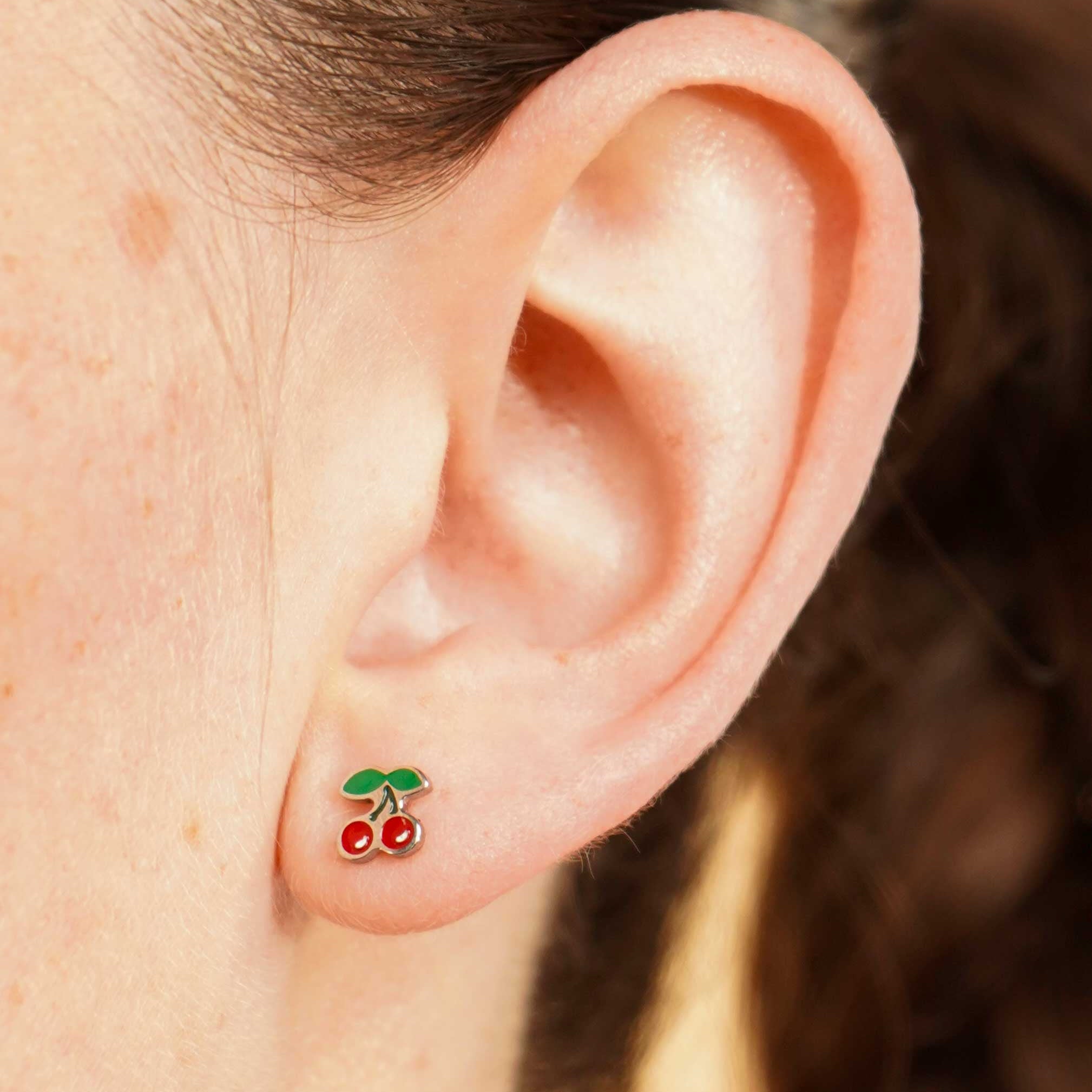 Close-up of an ear wearing a colorful enamel and titanium silver double cherry flat back stud earring with a blurred background