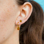 Close-up of an ear wearing a gold hoop with a cheeseburger-shaped charm on it with a blue background
