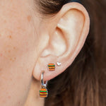 Close-up of an ear wearing a silver hoop with a cheeseburger-shaped charm on it with a blue background