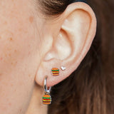 Close-up of an ear wearing a silver hoop with a cheeseburger-shaped charm on it with a blue background